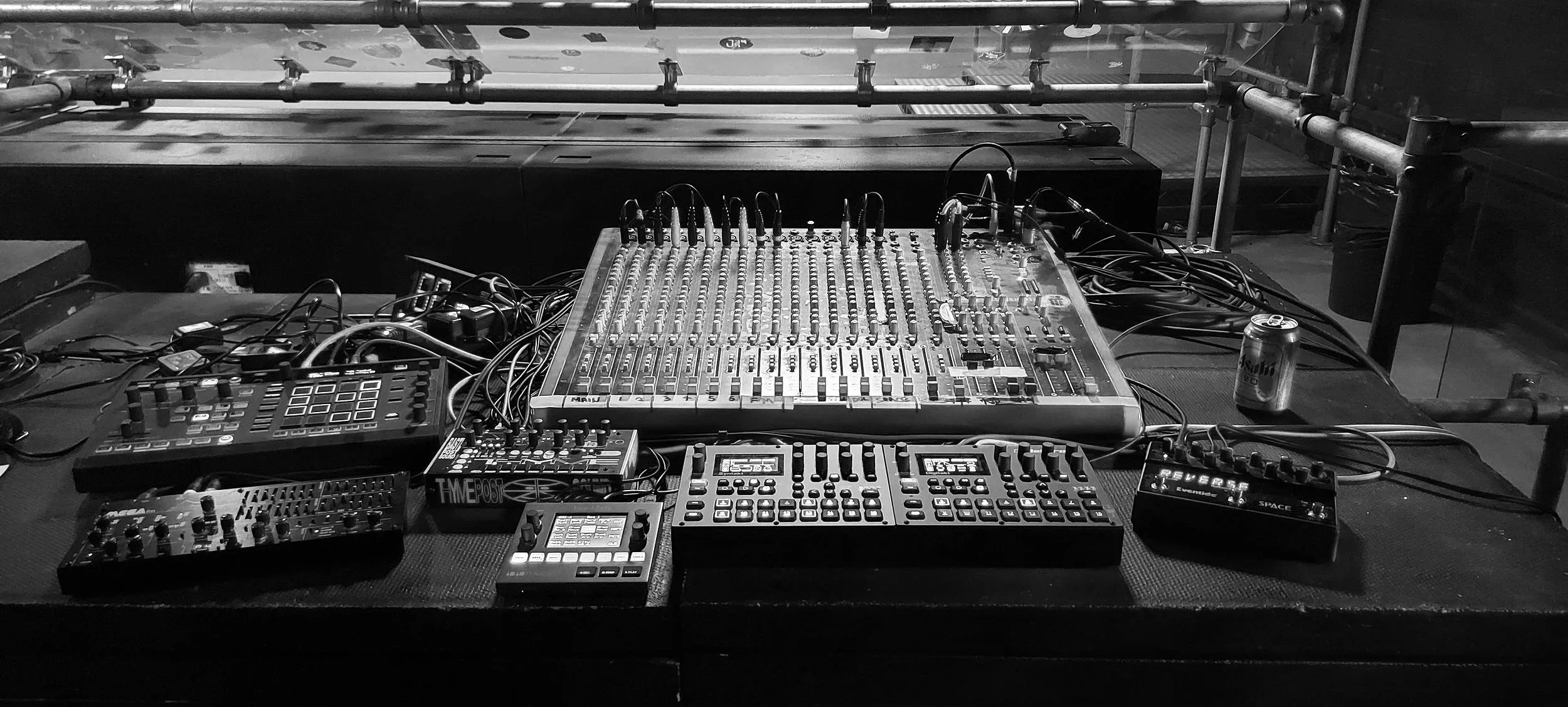 A DJ setup on a table with various audio equipment, including a mixing console, controllers, and electronic devices, with cables connected and a soda can to the right.
