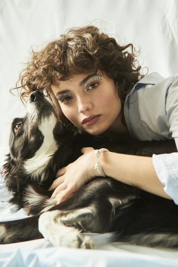 Mujer joven con maquillaje de purpurina junto a un perro de raza Border Collie