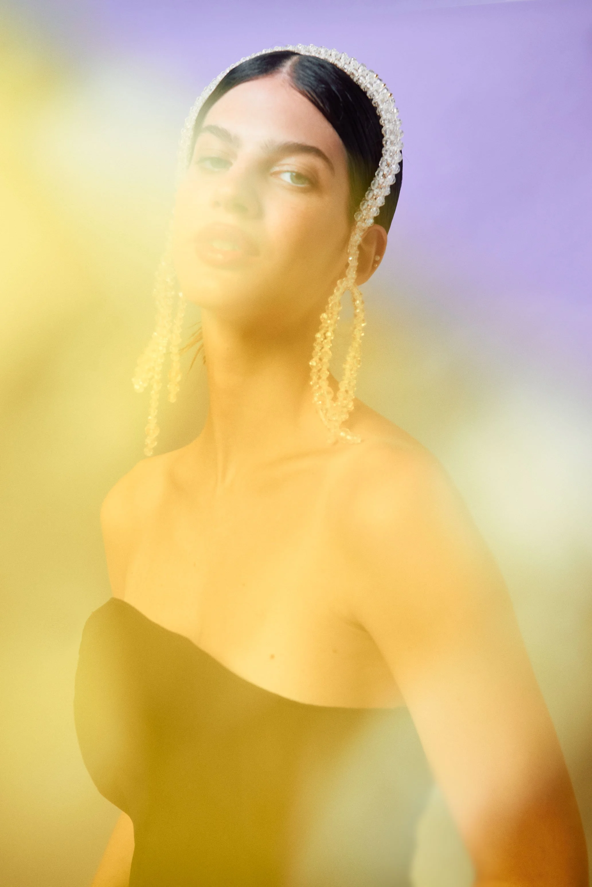 Retrato de mujer con estilo moderno, usando un vestido negro y accesorios de perlas, con un fondo colorido y difuso.