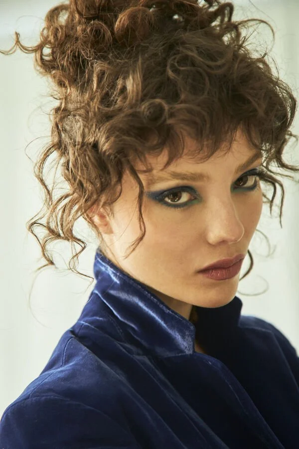 Retrato de una mujer con cabello rizado, maquillaje llamativo y ropa de terciopelo azul.