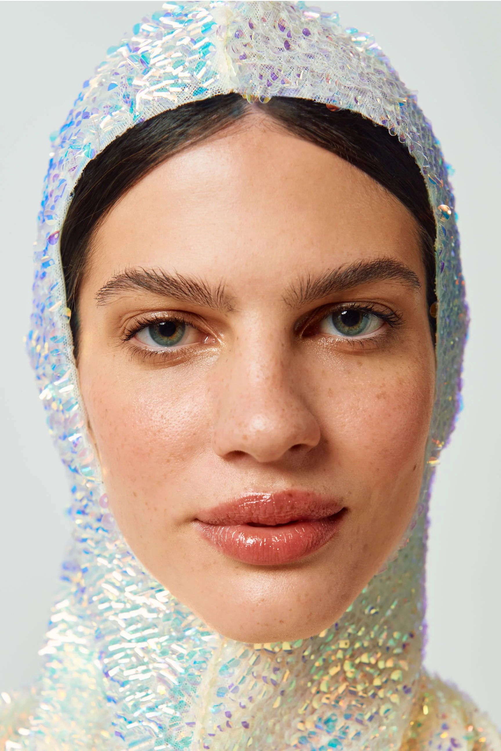 Retrato de una mujer con piel clara y ojos azules, usando una capucha de material holográfico y brillante.