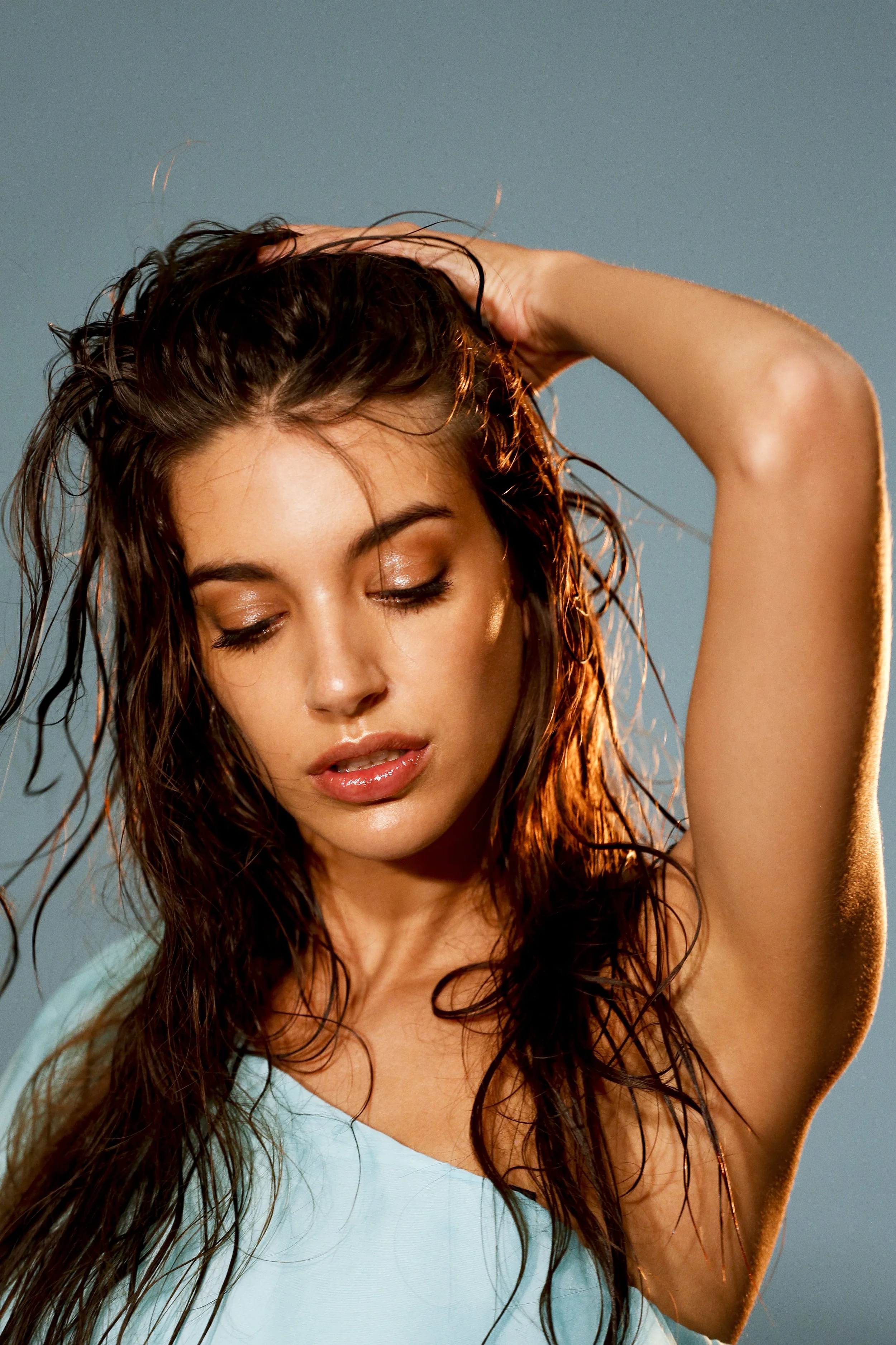 Mujer con cabello lluvioso y ojos cerrados, levantando un brazo y tocándose la cabeza