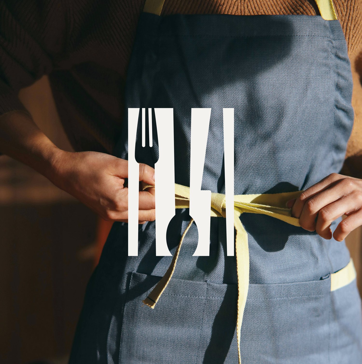 Person tying a yellow apron around their waist, over a gray uniform.