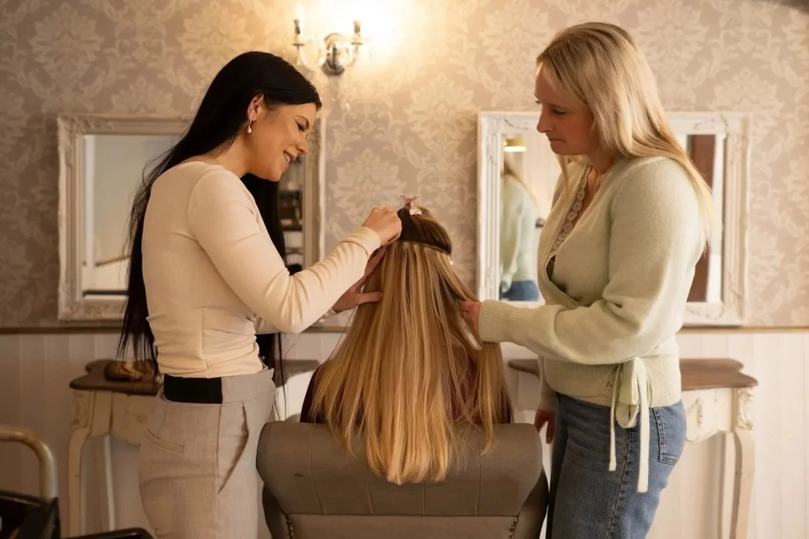 Woman in cream with long dark hair showing a trainee how to section hair and add hair extensions to a client