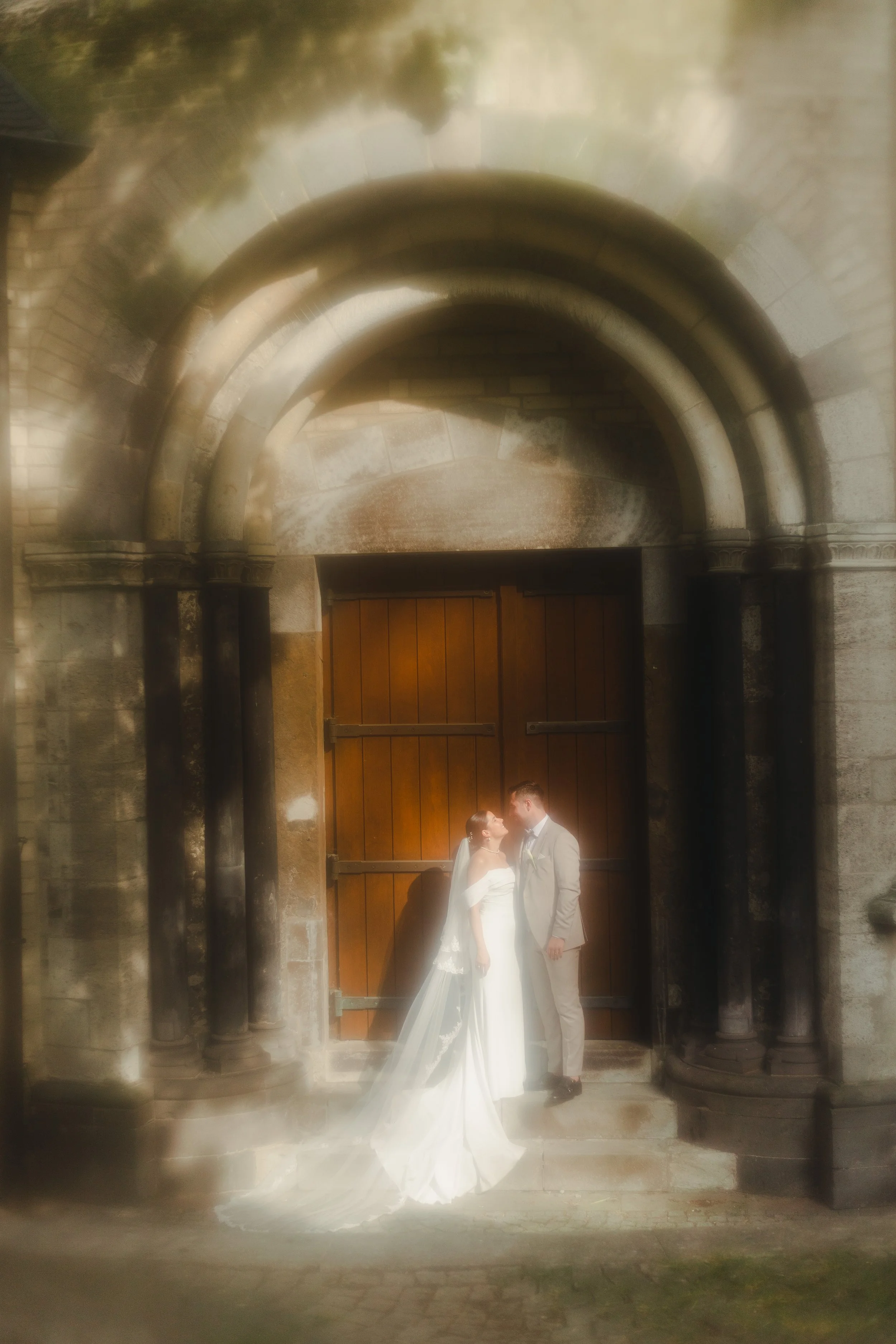 Ein Brautpaar vor einer alten Holztür, umgeben von einem steinernen Bogen, bei ihrer Hochzeit.