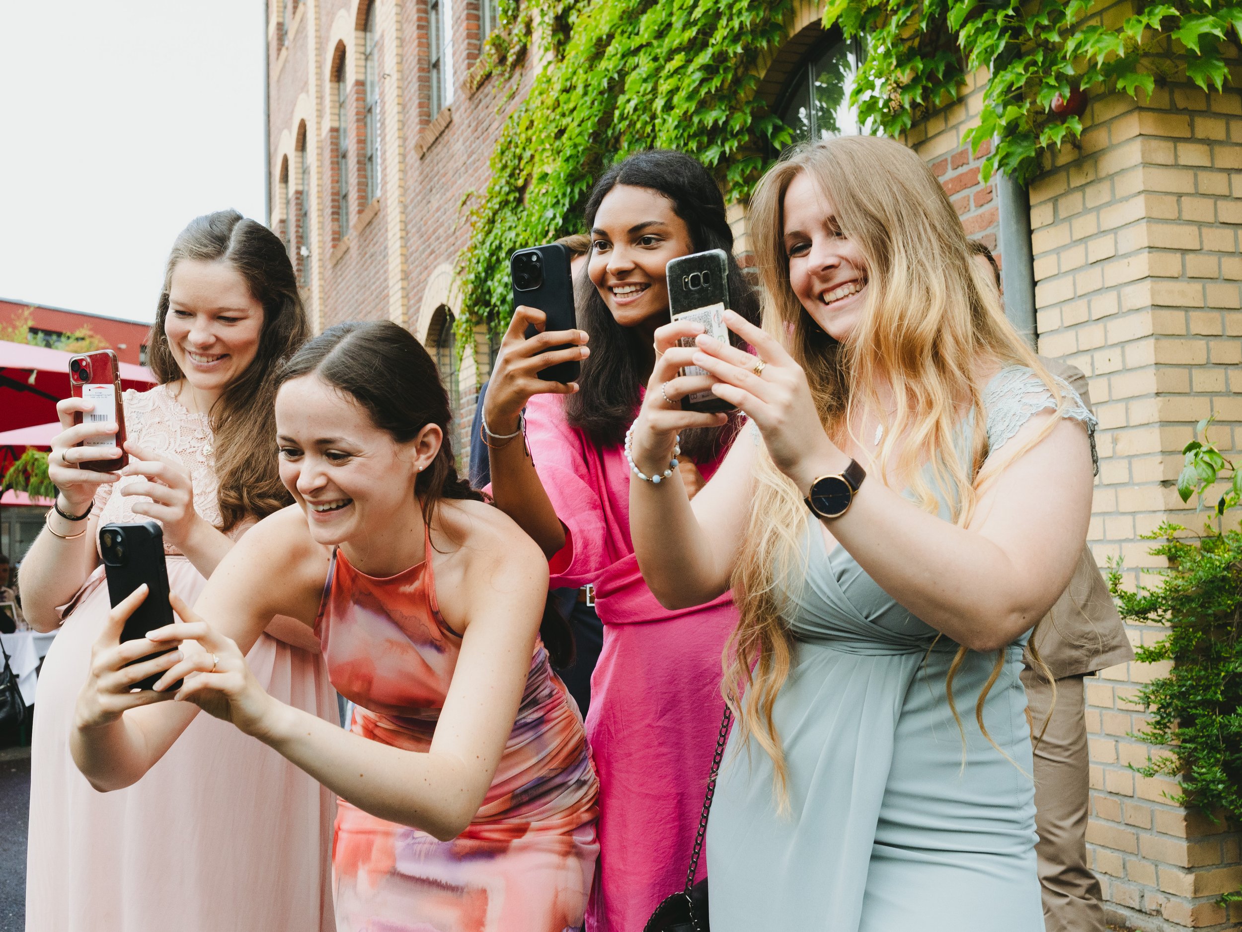 Fünf lachende Frauen im Garten, die Fotos mit Handys machen.