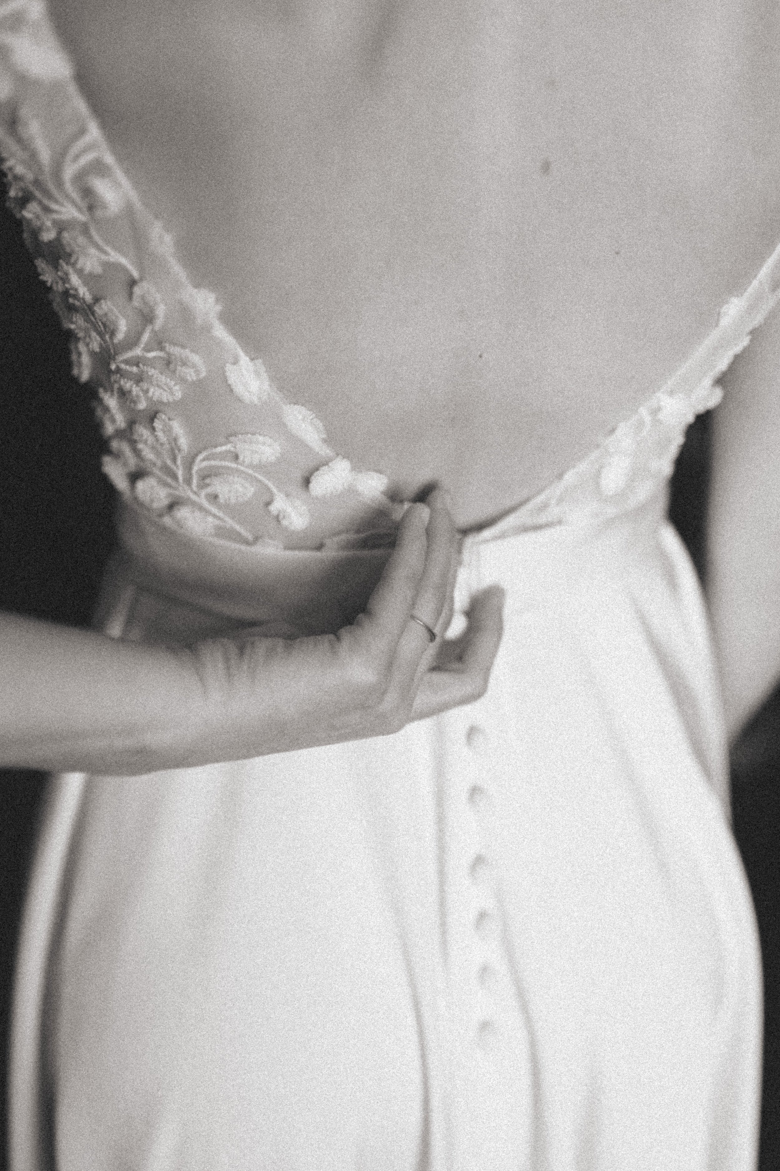 Nahaufnahme eines Brautkleids mit floraler Stickerei auf der Schulter, ein Hand hält das Kleid am Taillenbereich