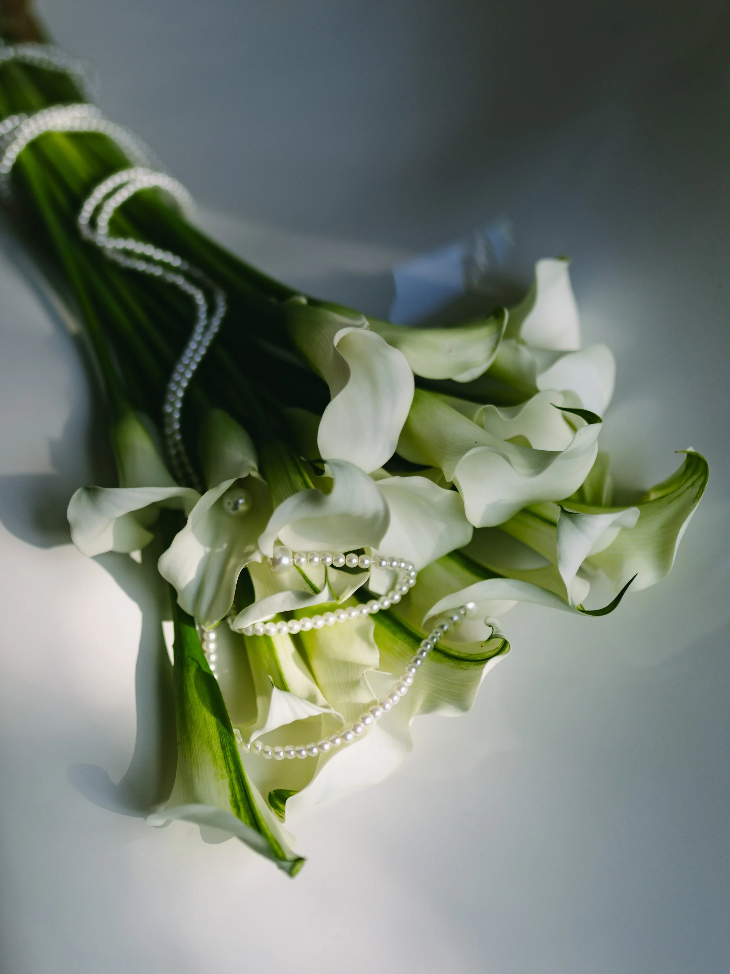 Weißer Blumenstrauß mit Perlenkette und weißen Perlen, auf weißem Hintergrund, natürliche Beleuchtung.
