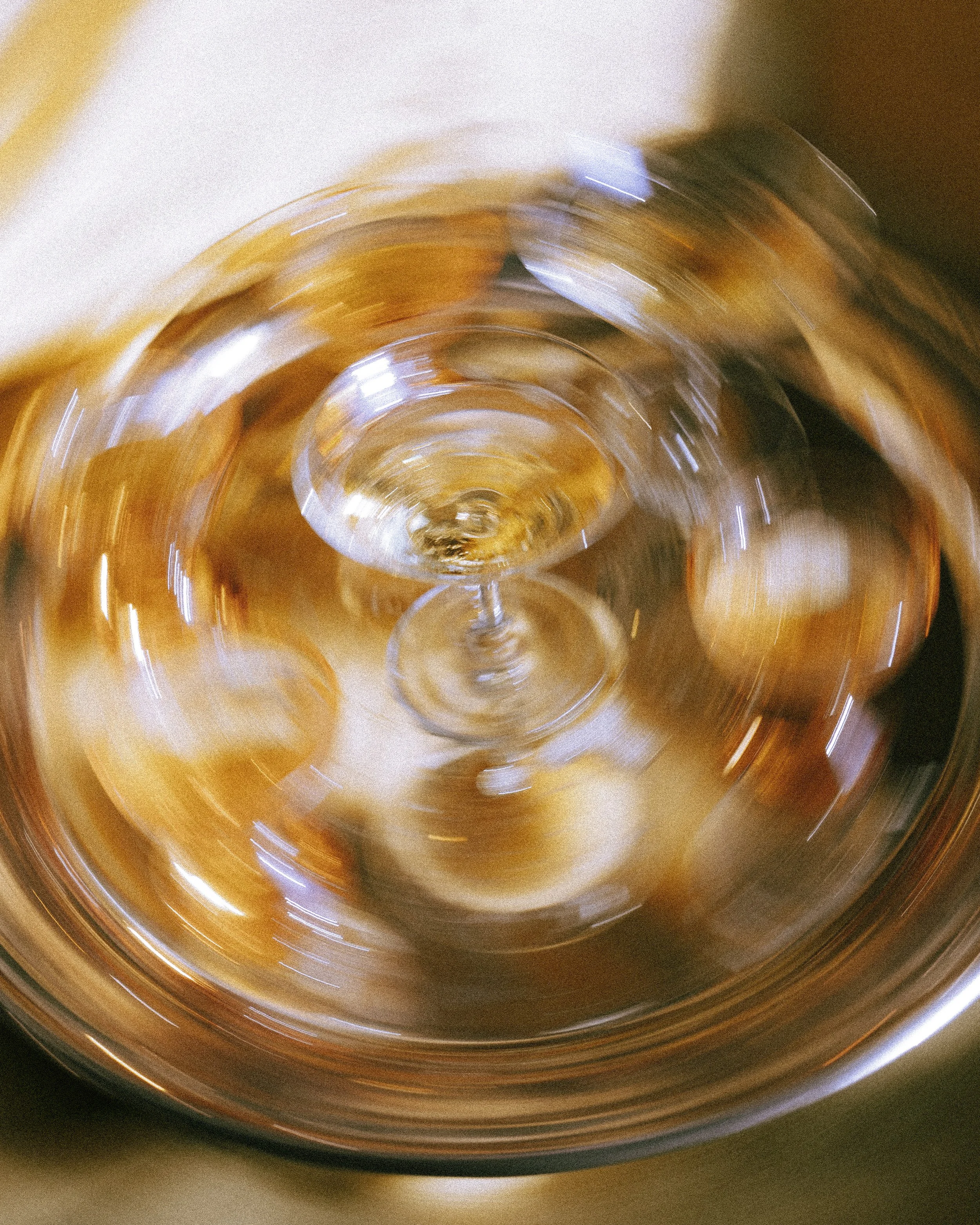 Verzerrtes Bild eines Weinglases auf einem Goldteller, das durch Bewegung unscharf wirkt.