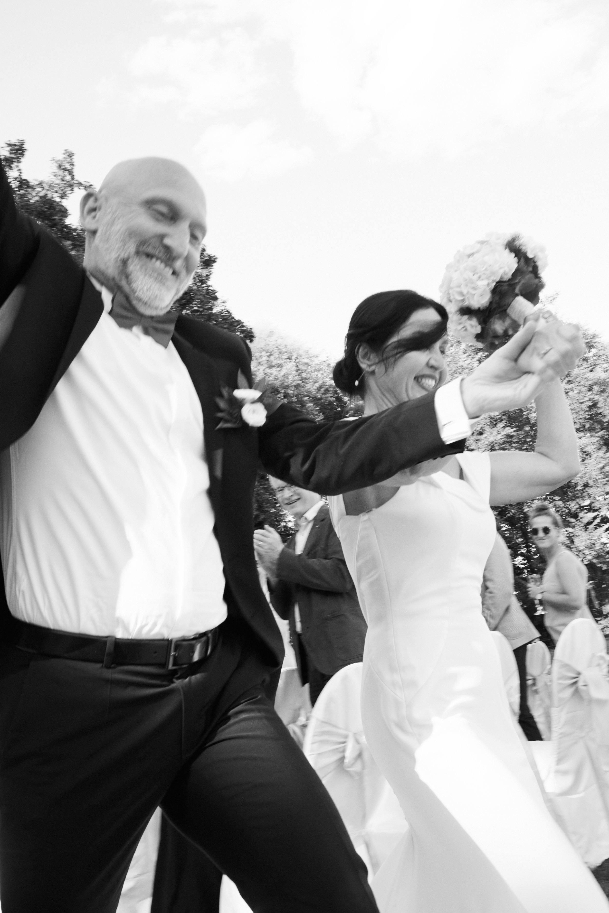 Ein glückliches Paar, das auf einer Hochzeit tanzt, mit dem Bräutigam und der Braut, die Champagnerflaschen heben, während Gäste im Hintergrund applaudieren.