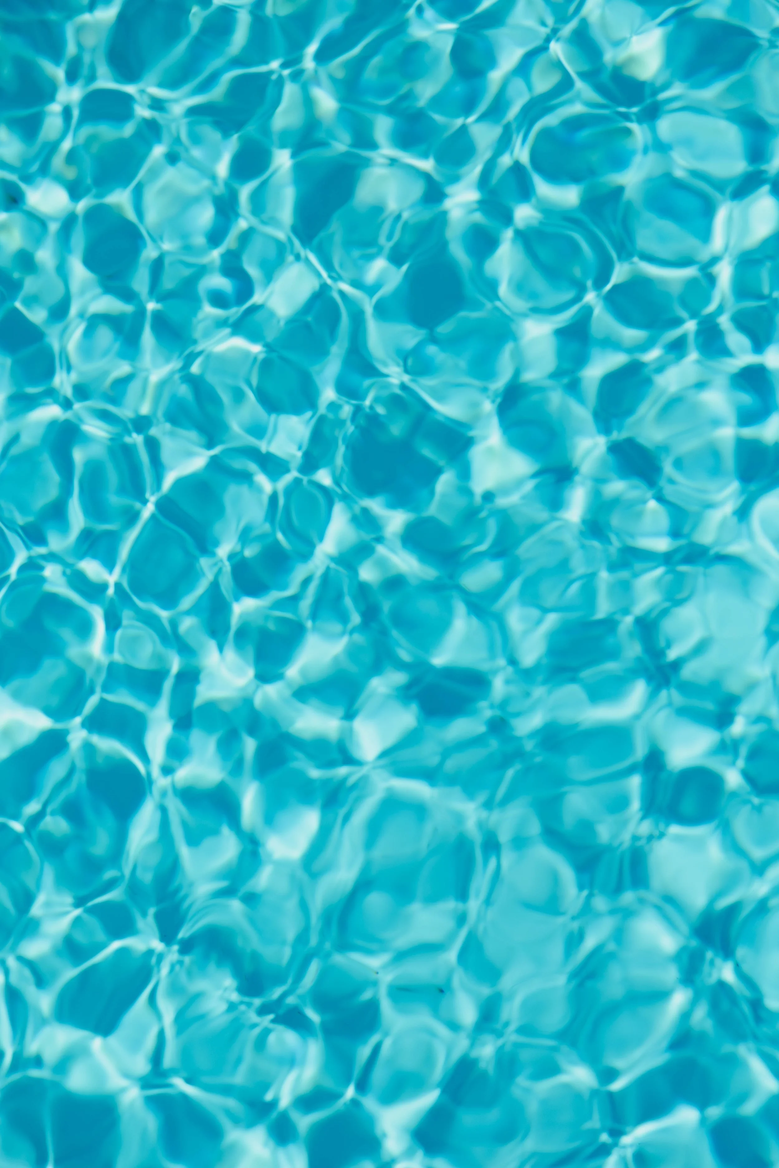 Blick auf die Wasseroberfläche eines Schwimmbeckens mit sichtbaren Lichtreflexionen und Wellenmustern.