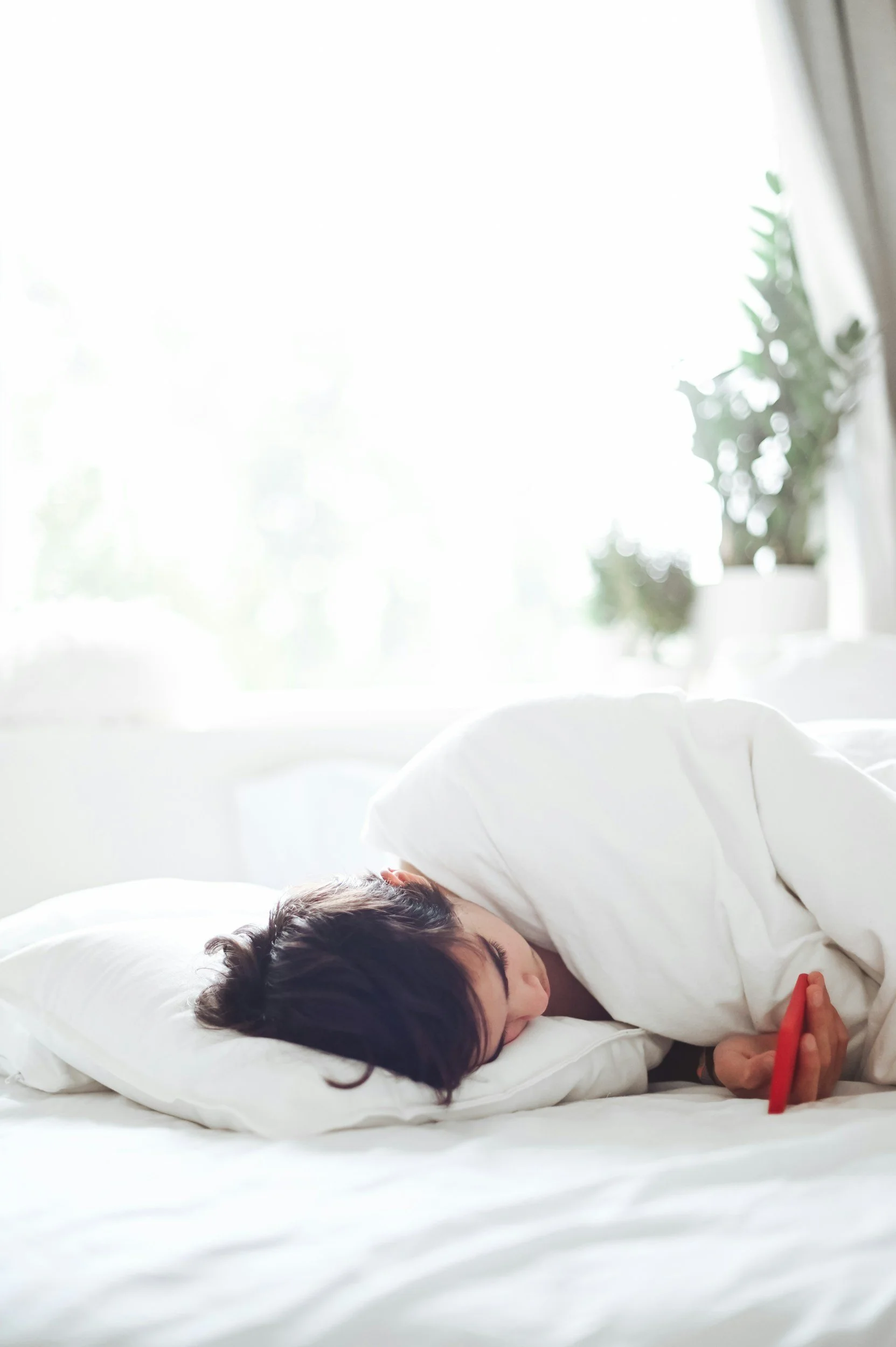 Een persoon ligt op een wit bed, onder een wit dekbed, met een kopje op de pillow.