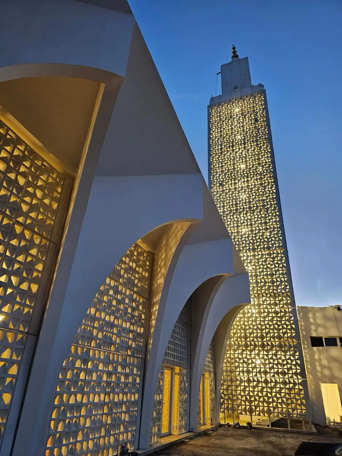 Discover our Mosque by night. 

The delicate white perforated screen, inspired by traditional Moroccan patterns, filters the sunlight and casts subtle, shifting shadows, giving the building a poetic and dynamic quality.

Mosque - Plage des Nations
Ne