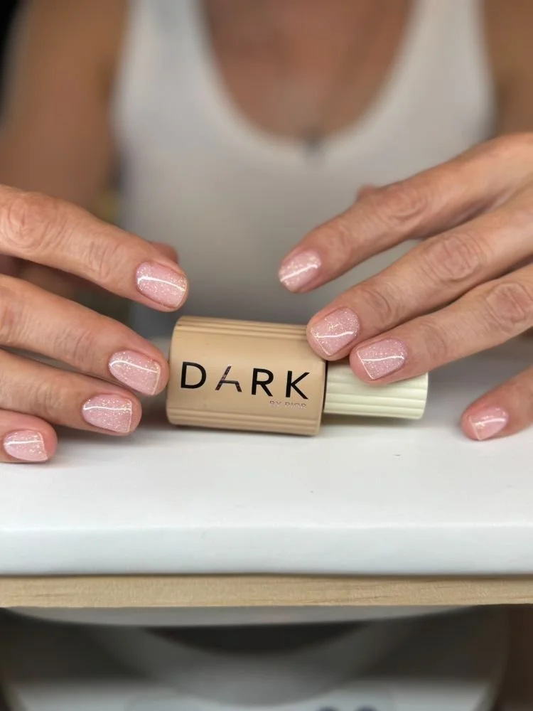 Person with painted nails holding a beige lipstick container labeled 'DARK by Dior'.