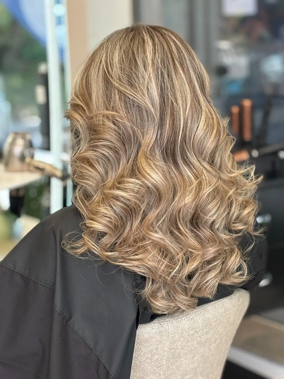 Close-up of a woman's blonde, wavy, shoulder-length hair, sitting in a salon.