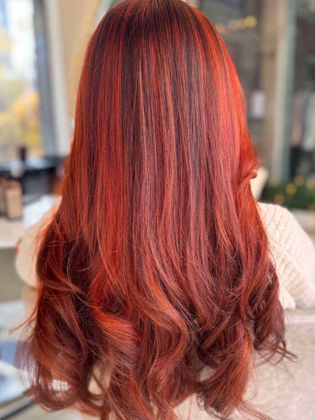 Back view of a woman with long, wavy, vibrant red hair.