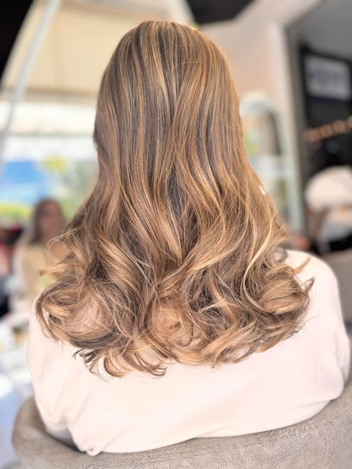 Back view of a woman with shoulder-length, wavy, honey-blonde hair.