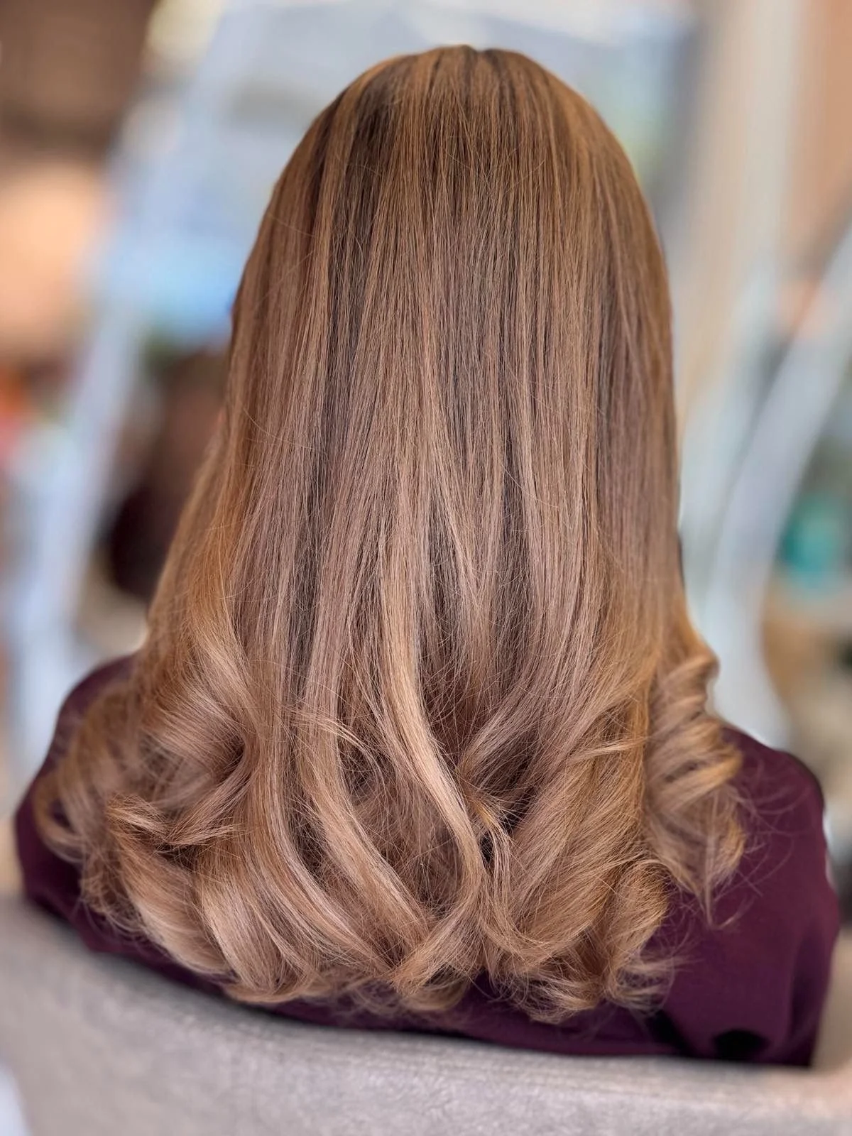 Back of woman's head showing shoulder-length, wavy, light brown hair with highlights.