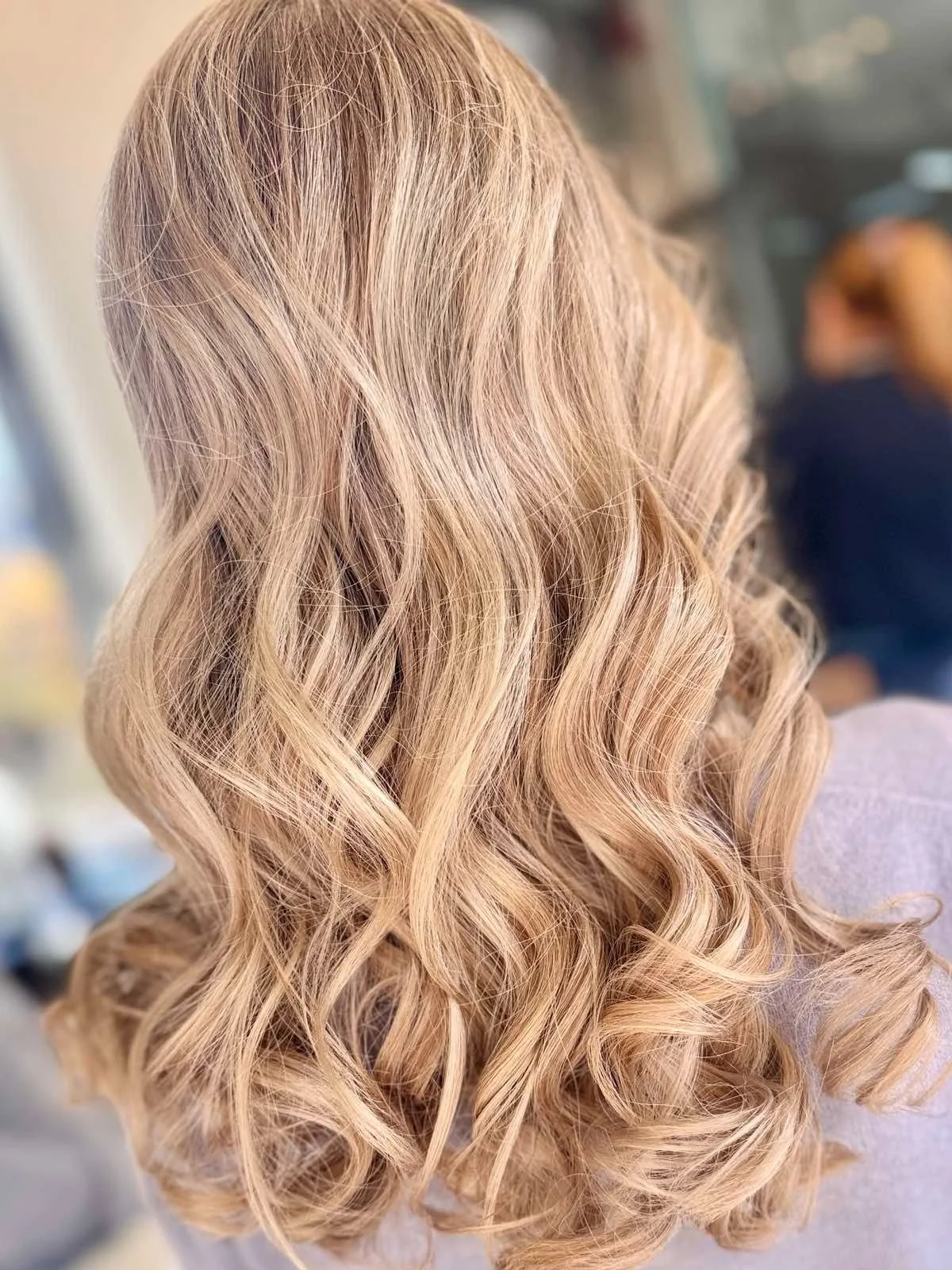Back view of a woman with shoulder-length, wavy blonde hair.