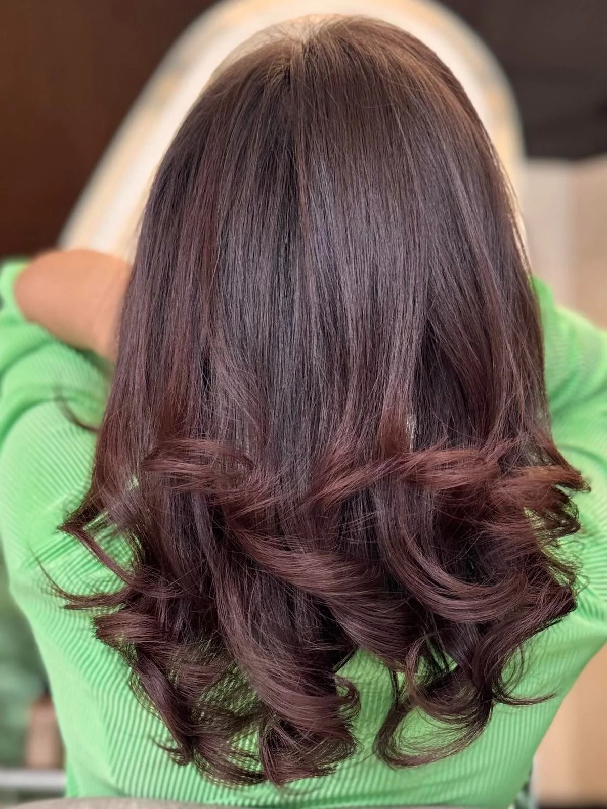 Top view of a woman with long, wavy, dark brown hair and reddish highlights, wearing a bright green shirt.