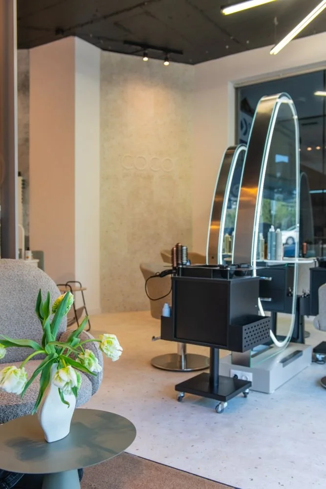 A modern hair salon with styling stations, mirrors, and a small table with white flowers in a vase.