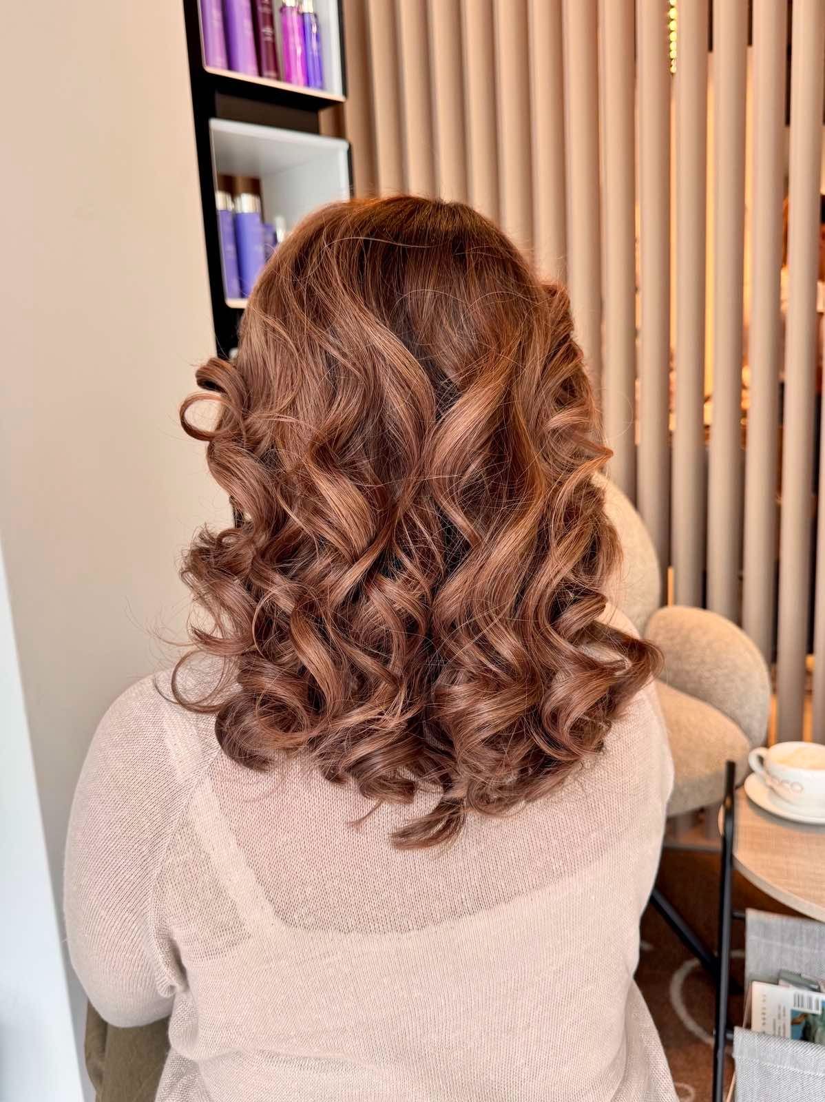 Back of a woman's head showing shoulder-length, curly, light brown hair.