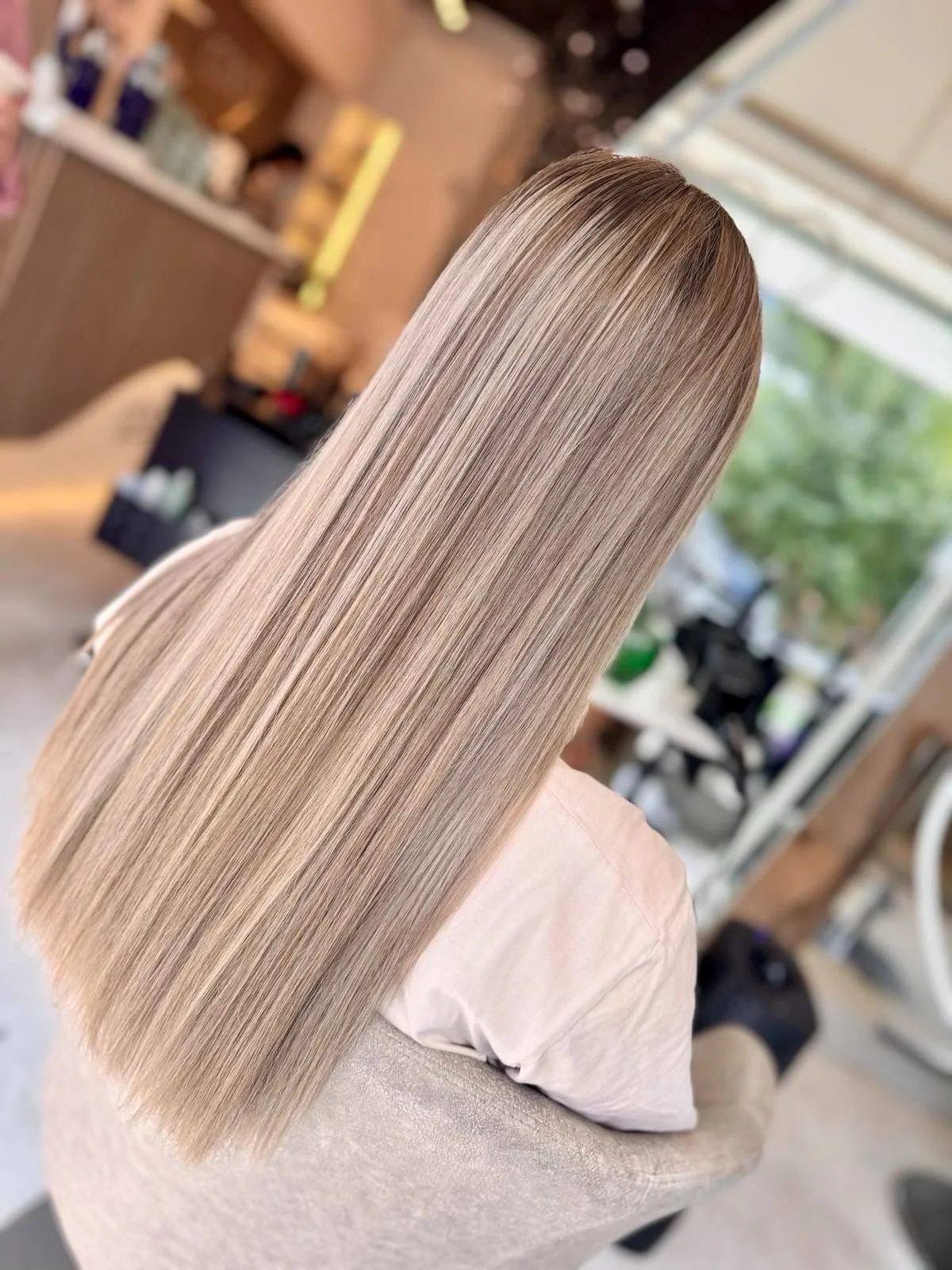Long straight blonde hair with highlights, seen from the back, in a hair salon setting.