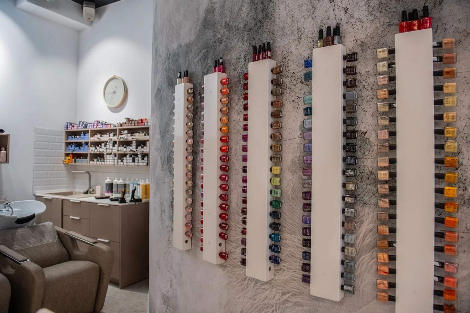 Display of nail polish bottles arranged by color on white panels in a nail salon.