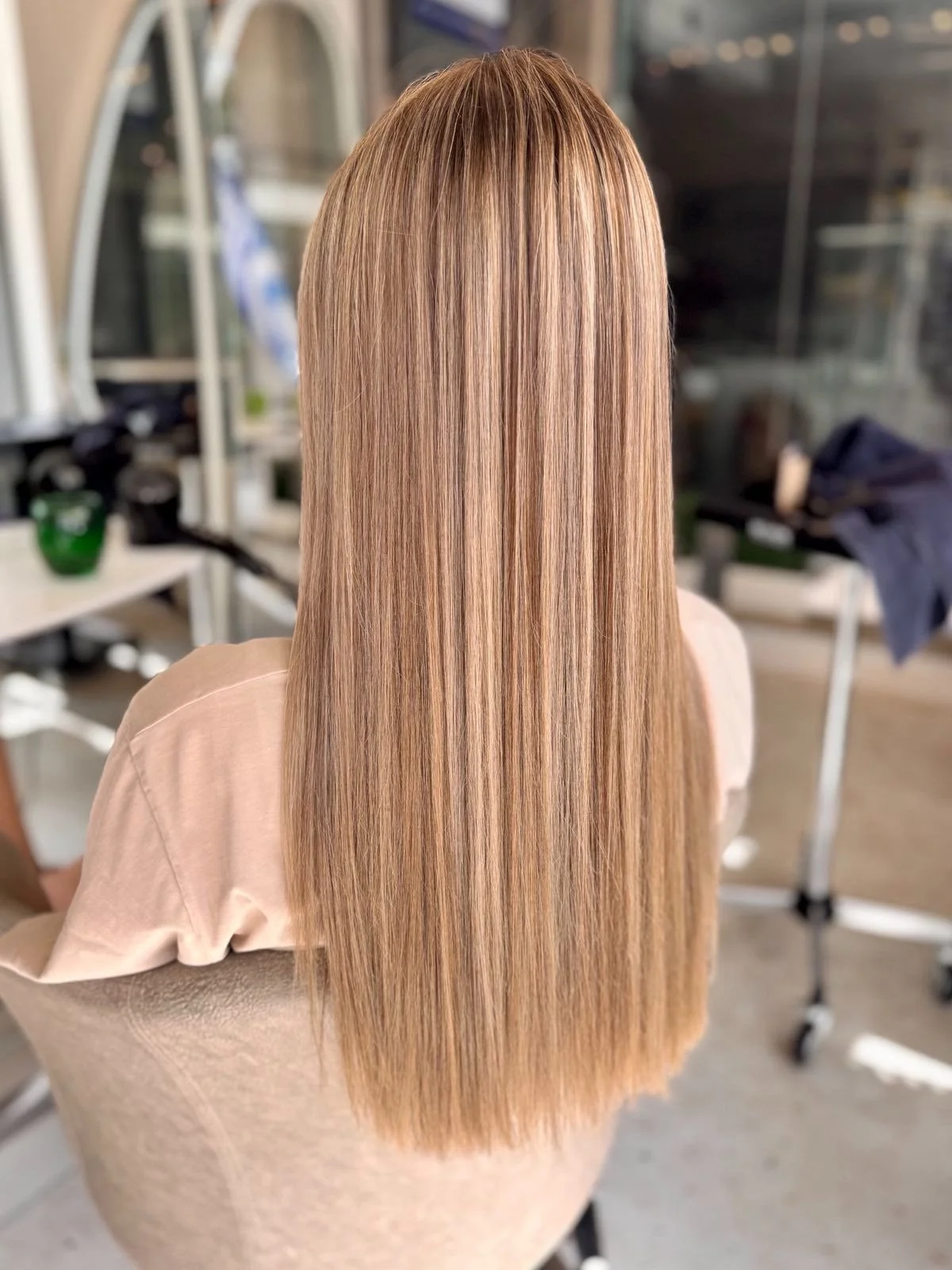 Back view of a woman with long, straight, blonde hair in a salon.