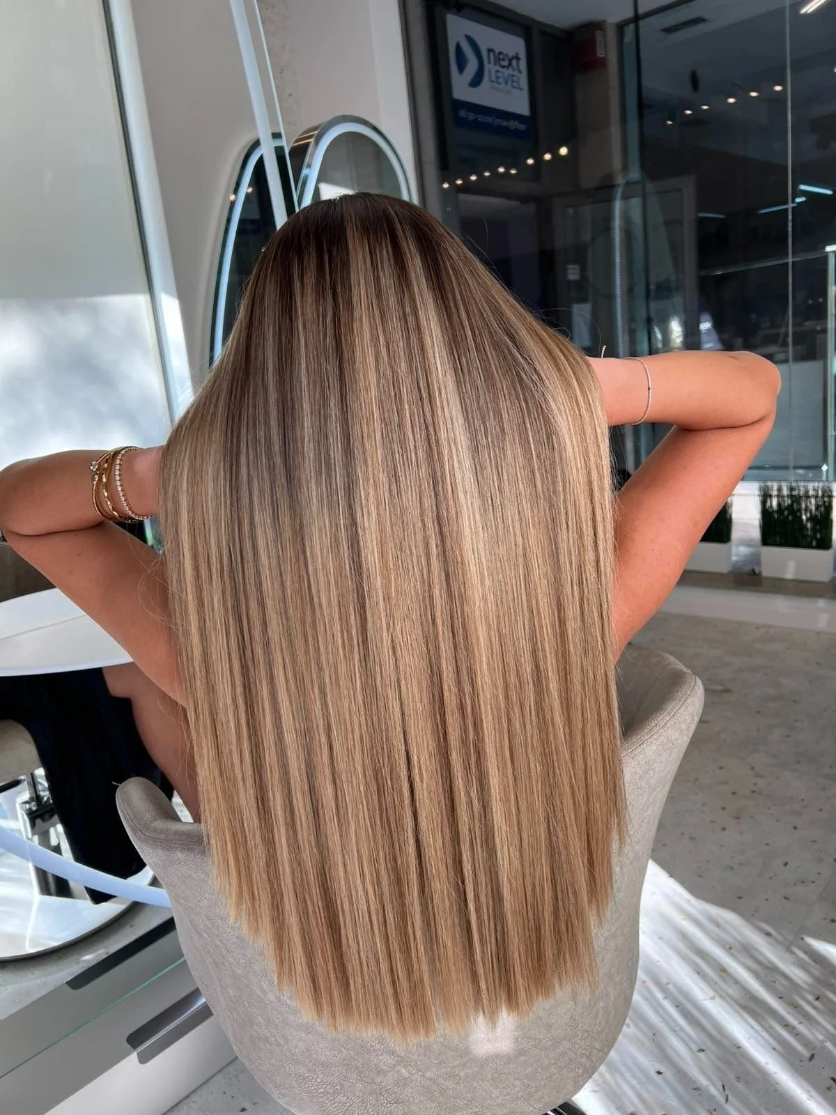 Back view of a woman with long, straight, blonde hair sitting in a salon chair.
