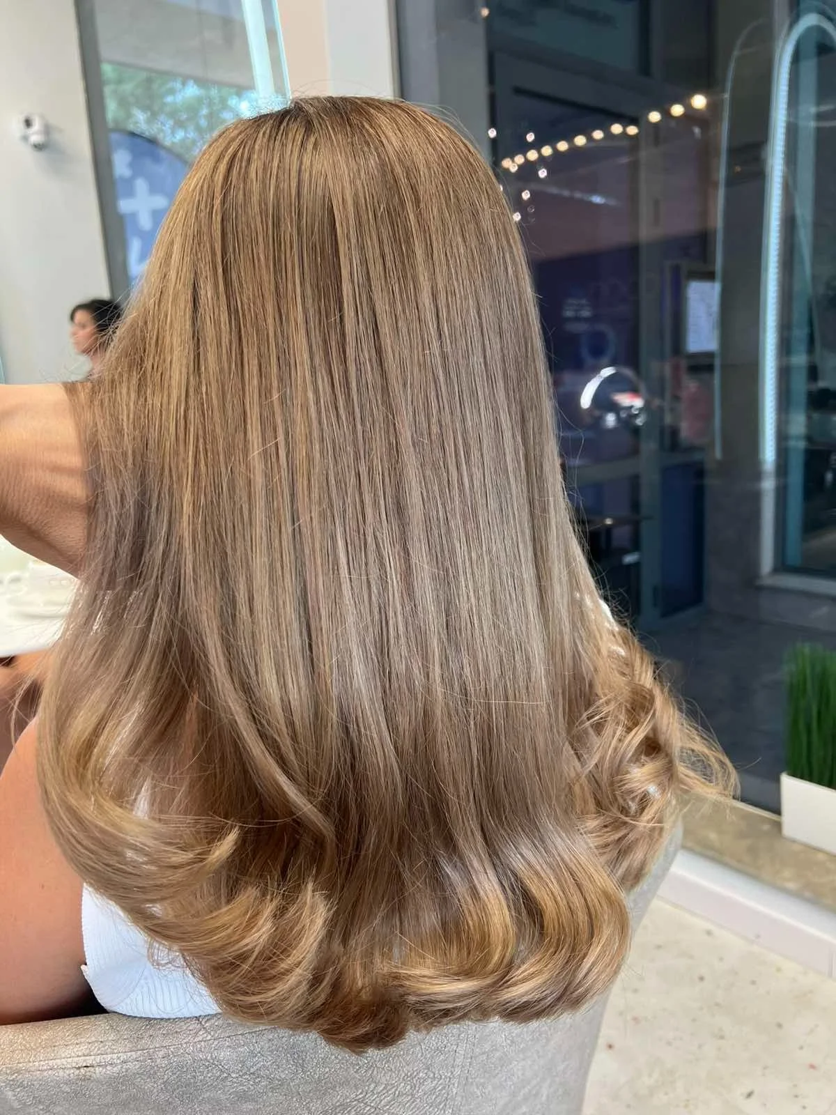 Back view of a woman with long, blonde hair styled with loose curls inside a salon.