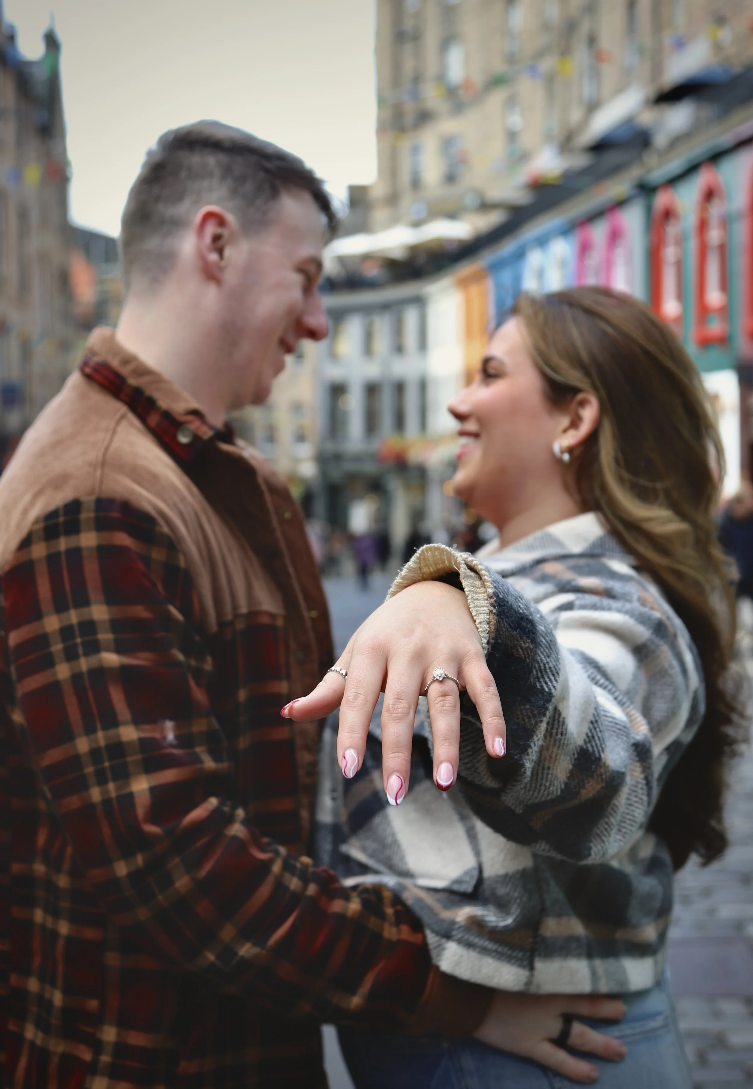 A couple smiling at each other with their hands on each other's waist. The woman shows her engagement ring.