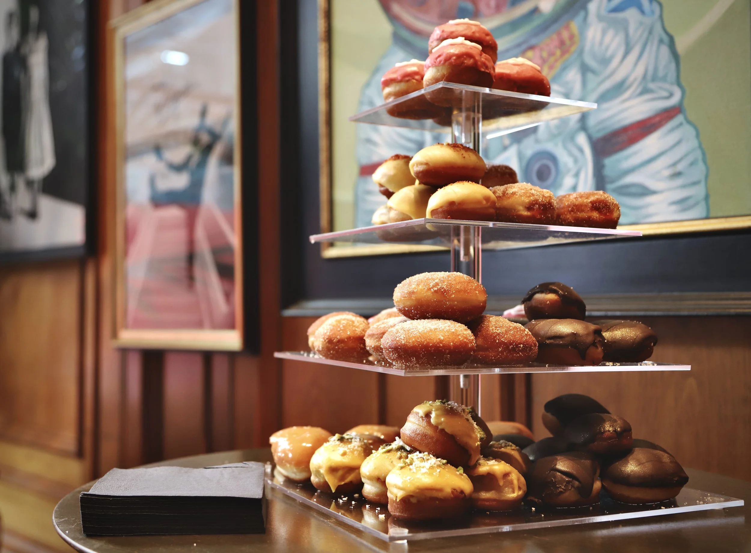 A tiered stand displaying various donuts with different glazes and toppings inside a cafe or bakery.