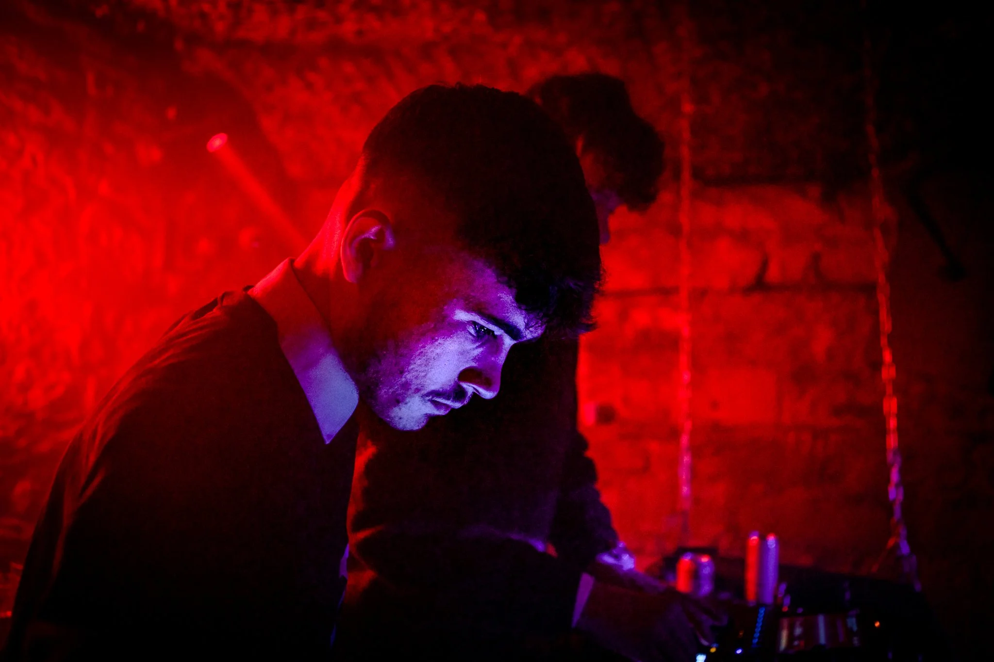 DJ with headphones in a dark, red-lit room, operating sound equipment.