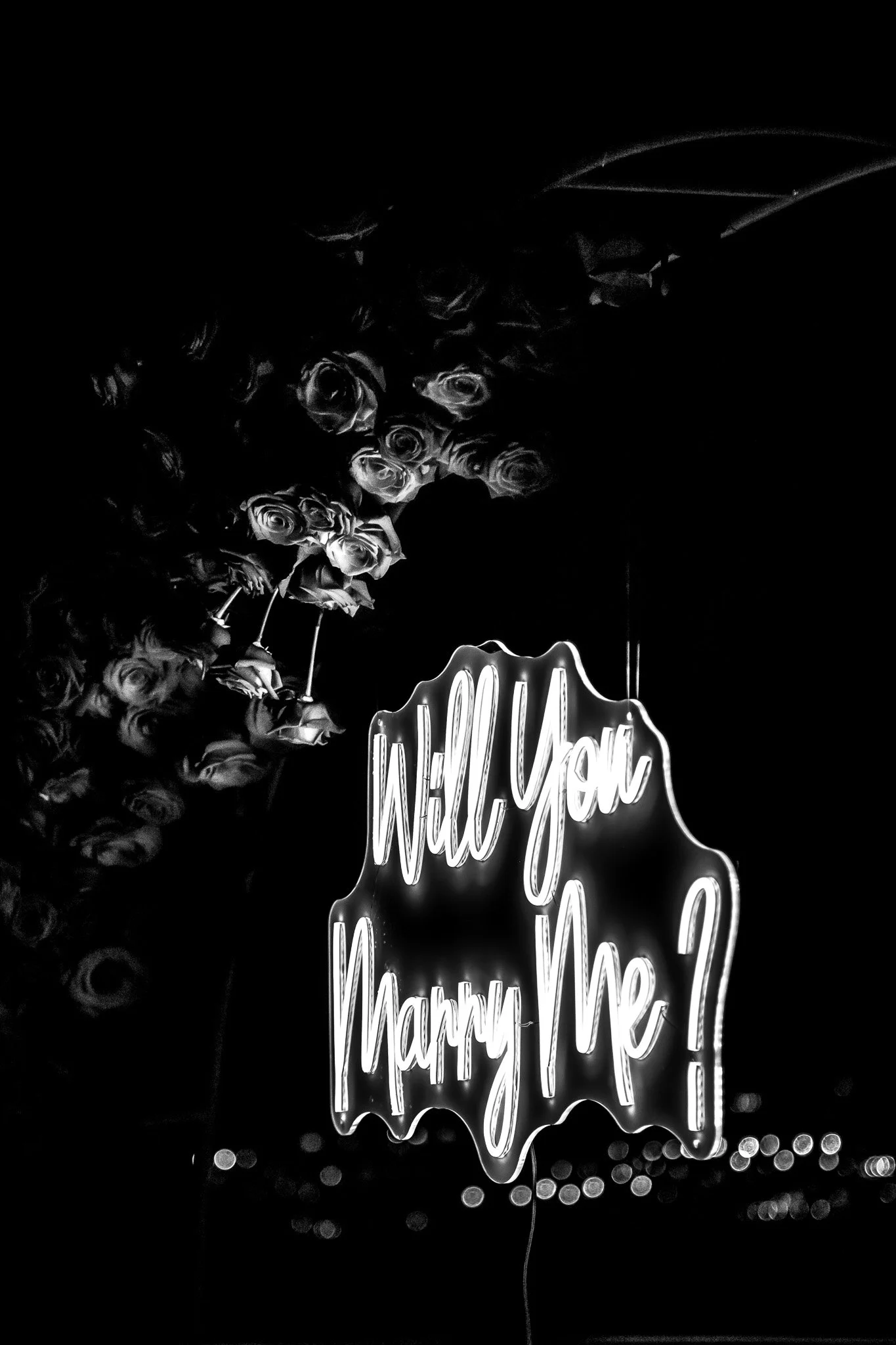 Neon sign that says 'Will You Marry Me?' with a bouquet of roses in the background