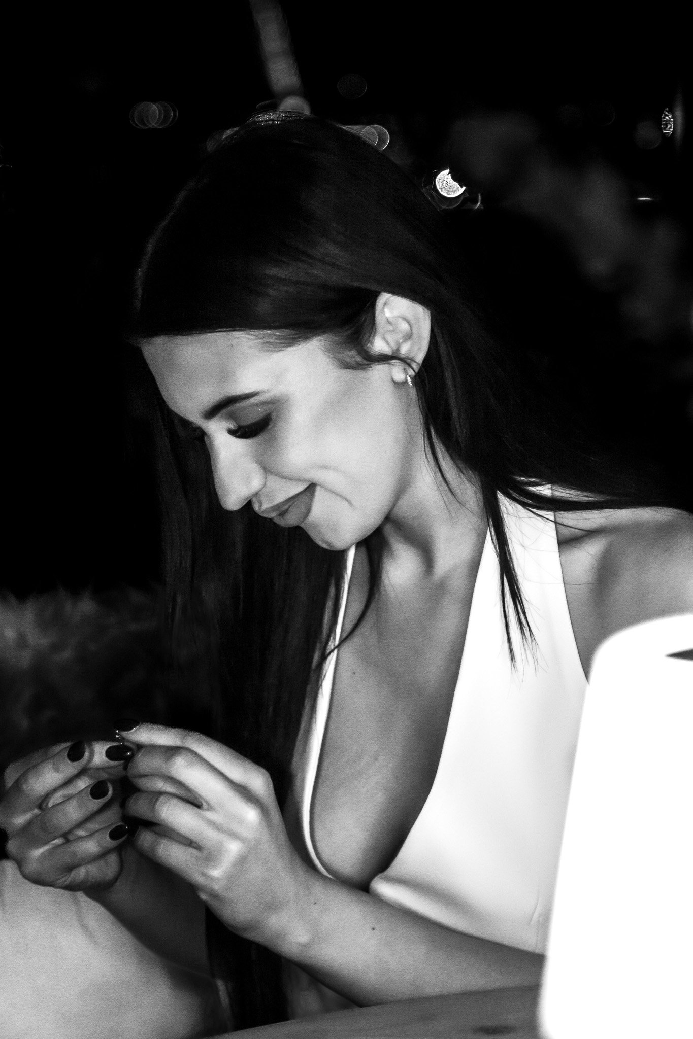 A black-and-white photo of a woman with long dark hair, wearing a sleeveless top, looking down and smiling while holding someone's hands.