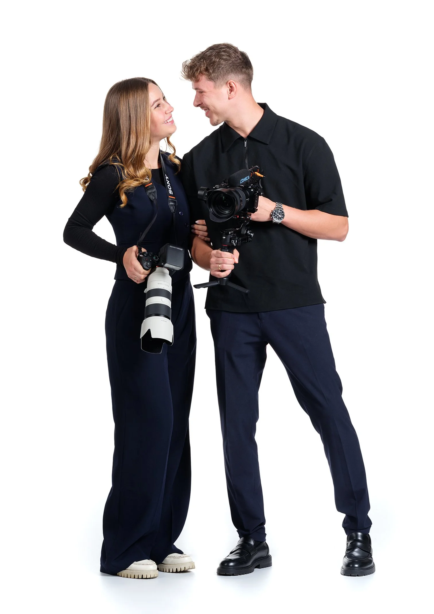 Ein Mann und eine Frau, beide mit Kameras, schauen sich an und lächeln.