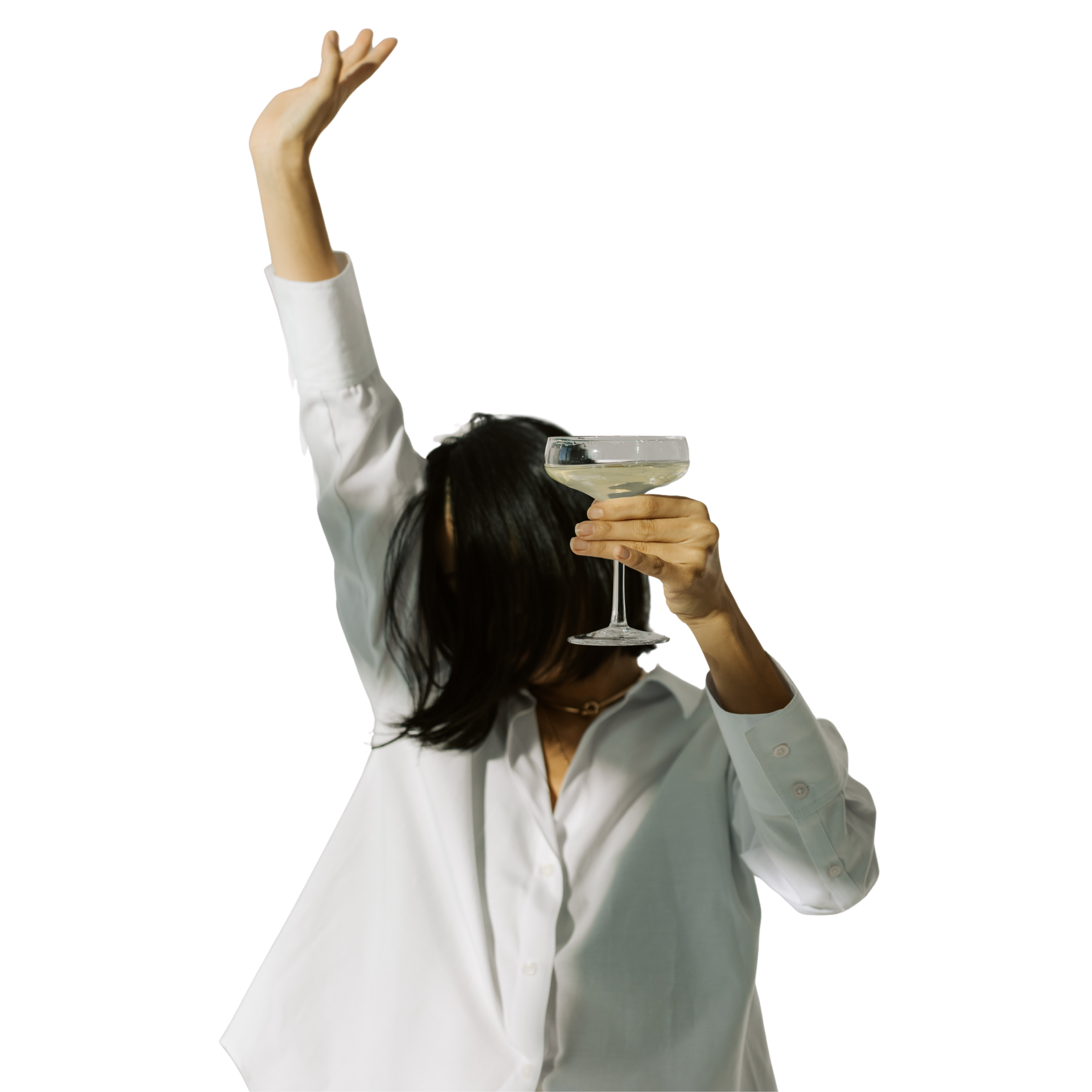 A person with dark hair in a white shirt holding a martini glass in front of their face and raising one arm in the air.