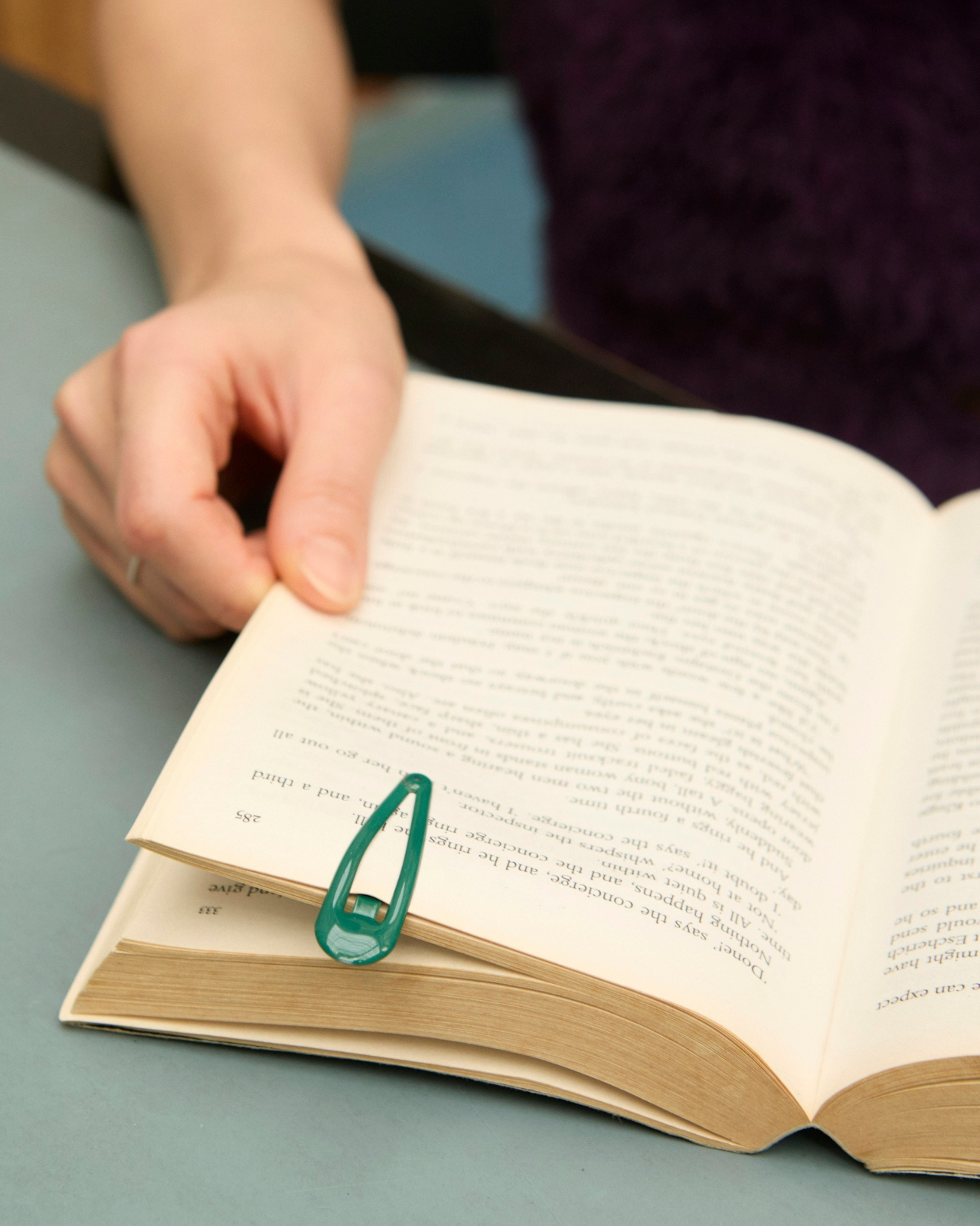 Person turning page of open book with paperclip on the page, sitting at a table.