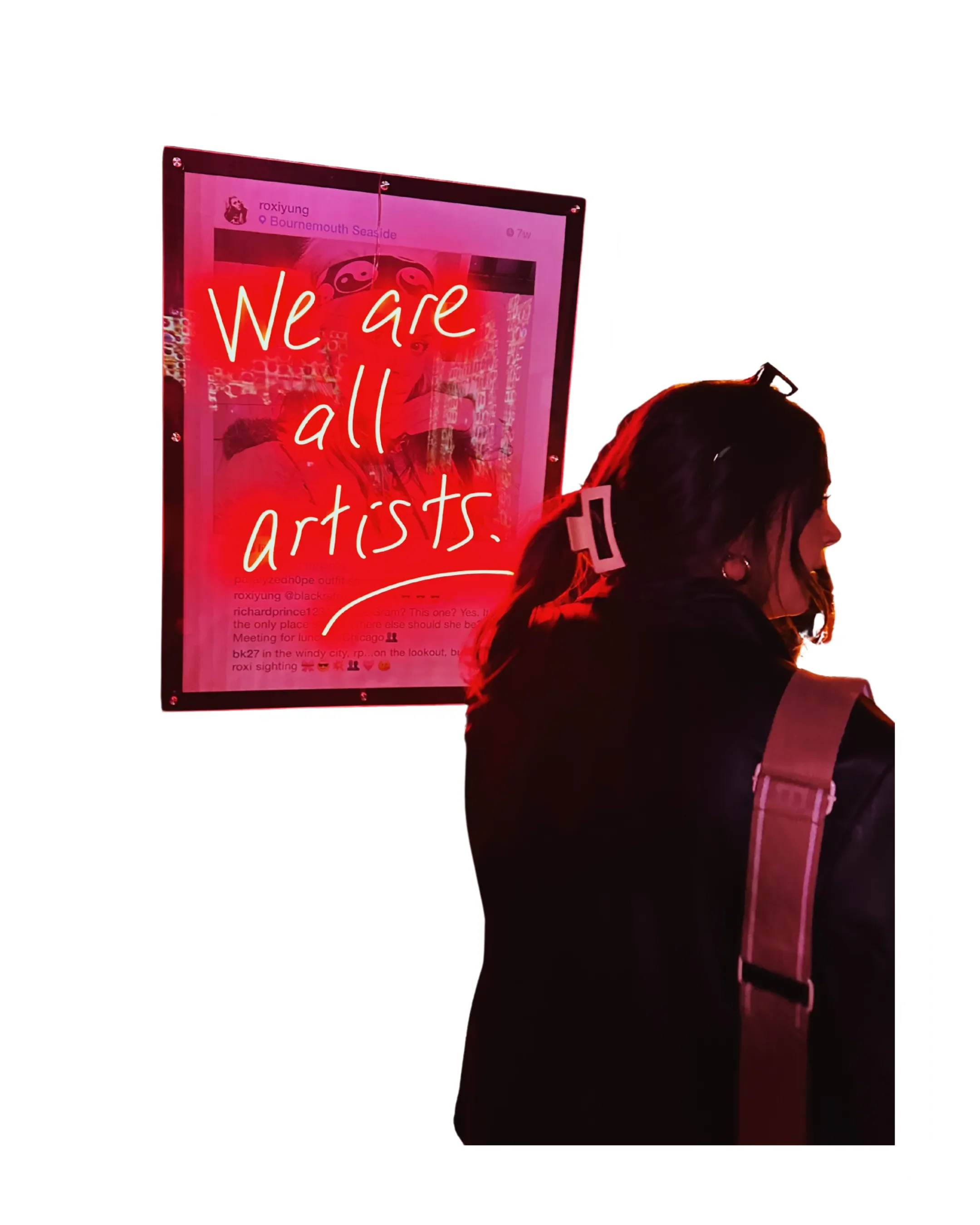 A person with shoulder-length hair and a backpack standing in front of a pink-lit digital sign that reads, 'We are all artists.'