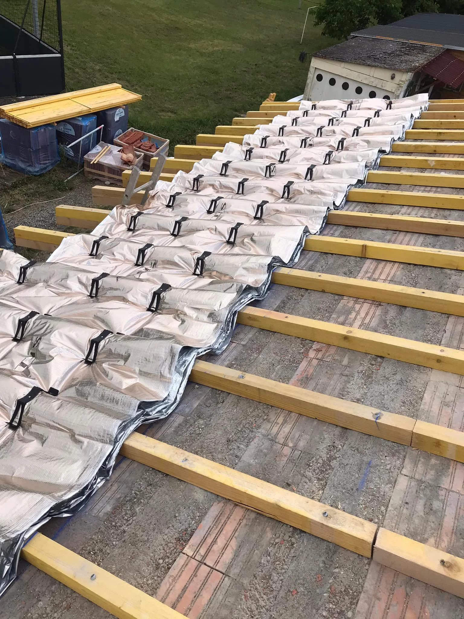 Travaux de construction avec des poutres en bois posées sur un sol en brique, recouvertes de membranes isolantes plissées, dans un cadre de bâtiment résidentiel.