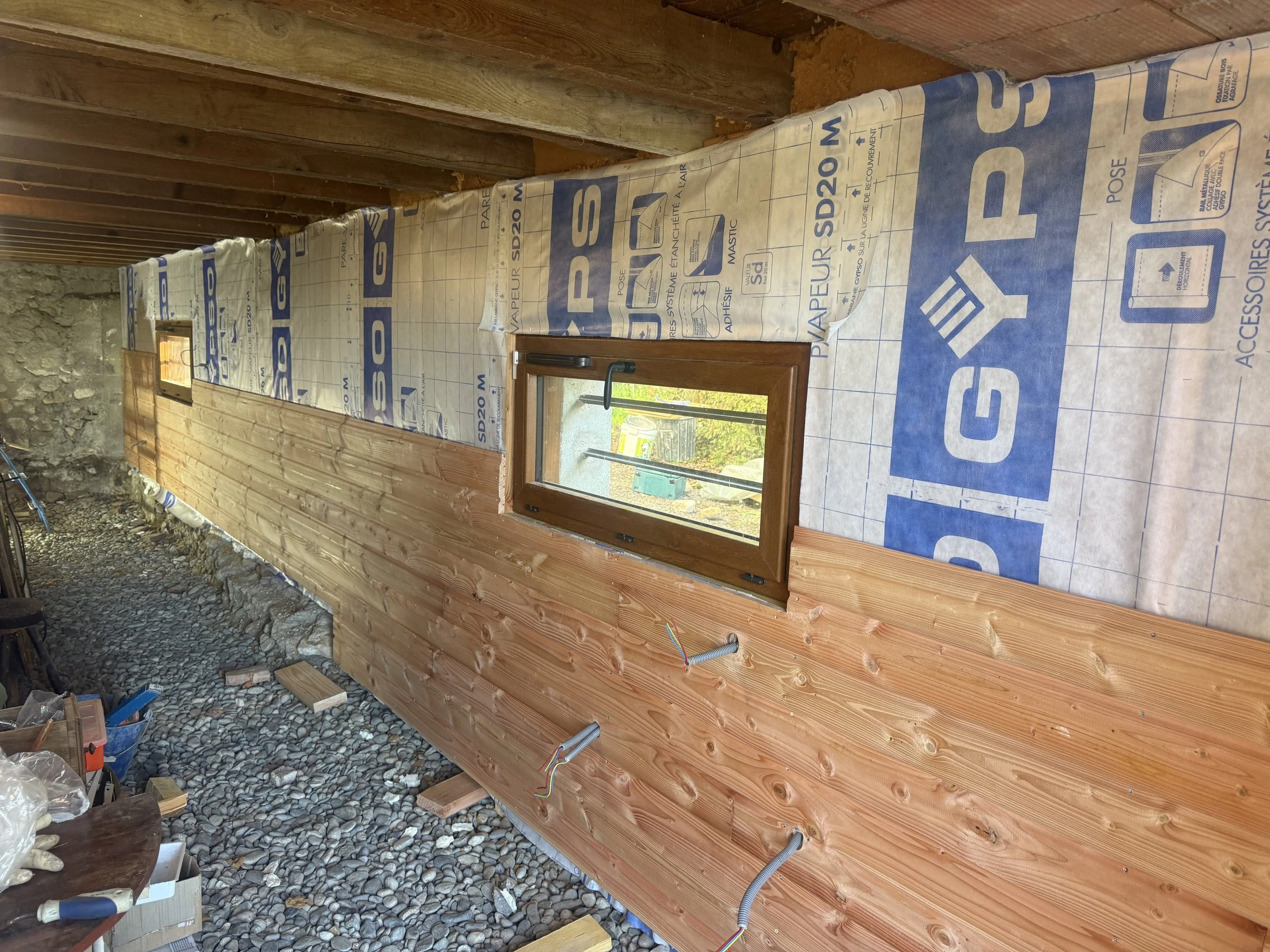 Intérieur d'une construction en bois avec du film d'isolant sur le mur et une petite fenêtre