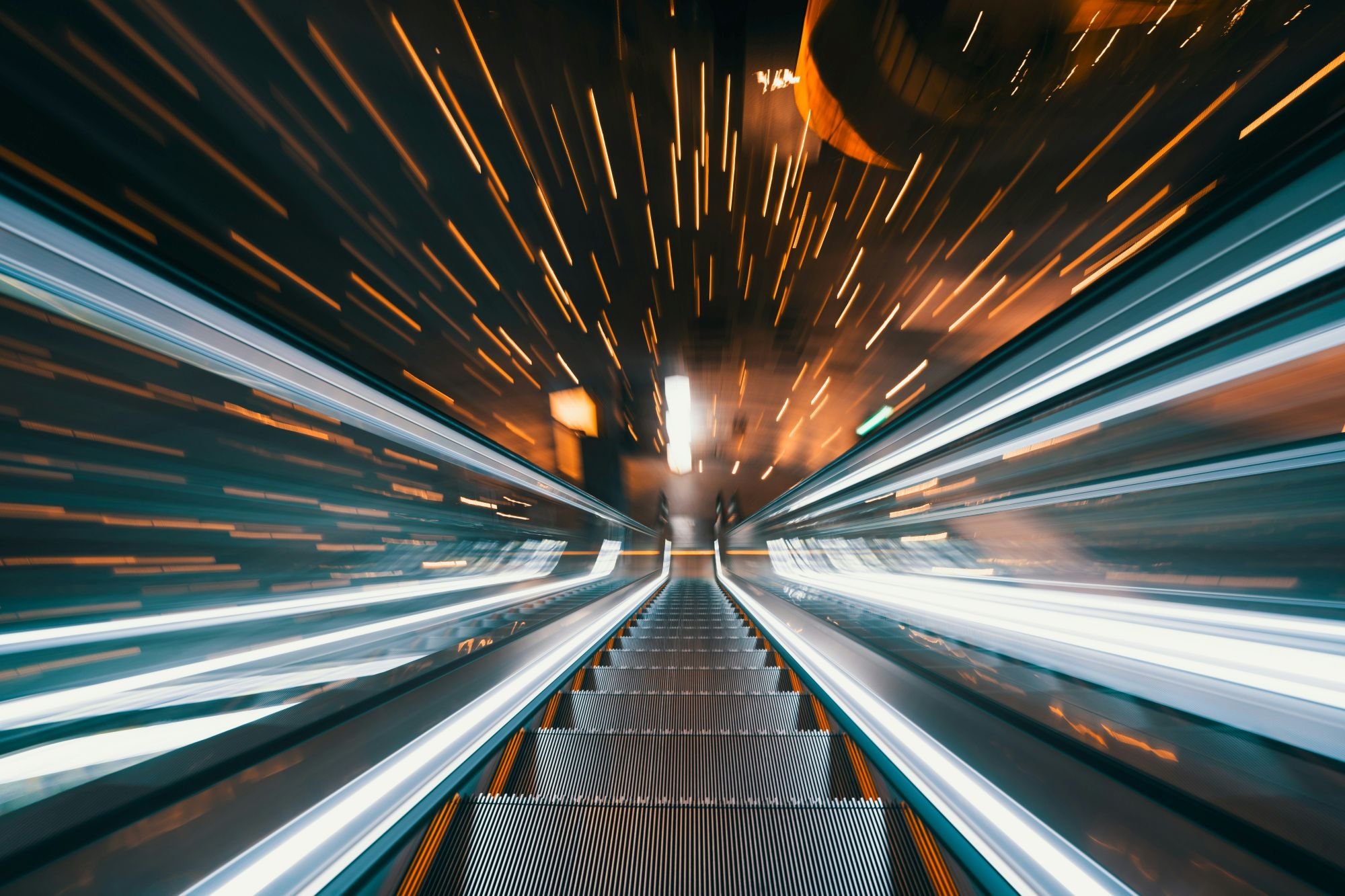 A long exposure photograph of moving train lights taken from the front on an escalator.