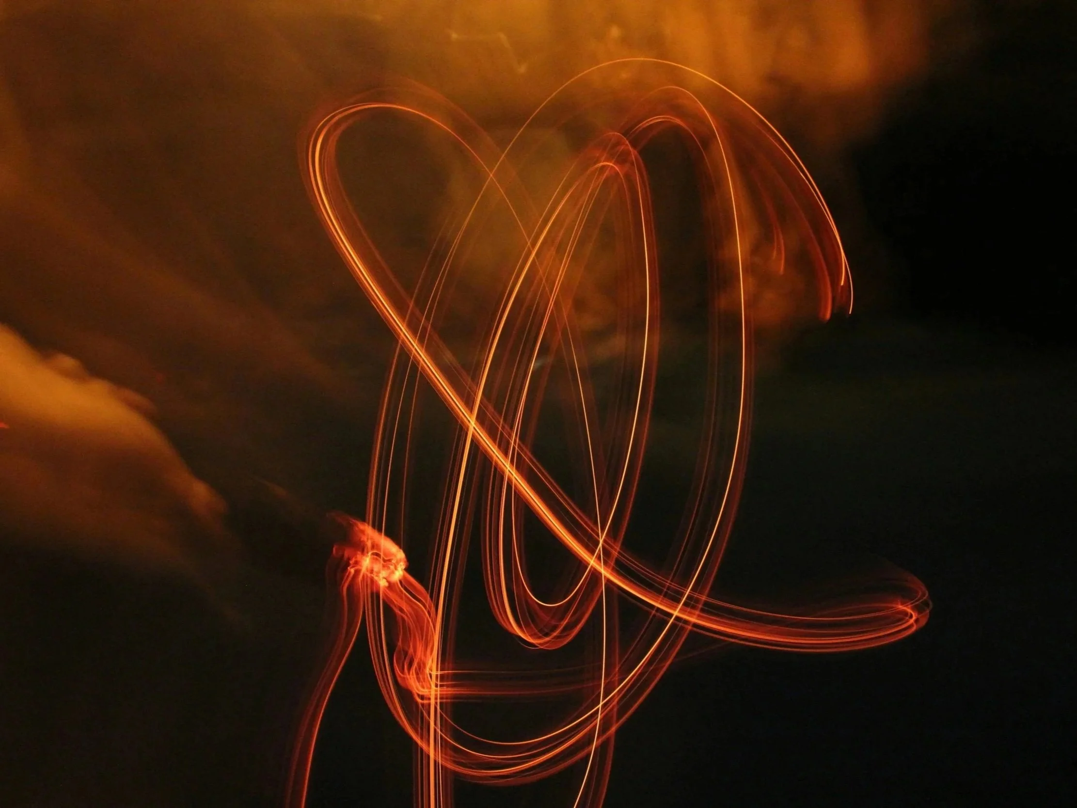Abstract light painting with swirling lines of orange light against a dark sky with some clouds.