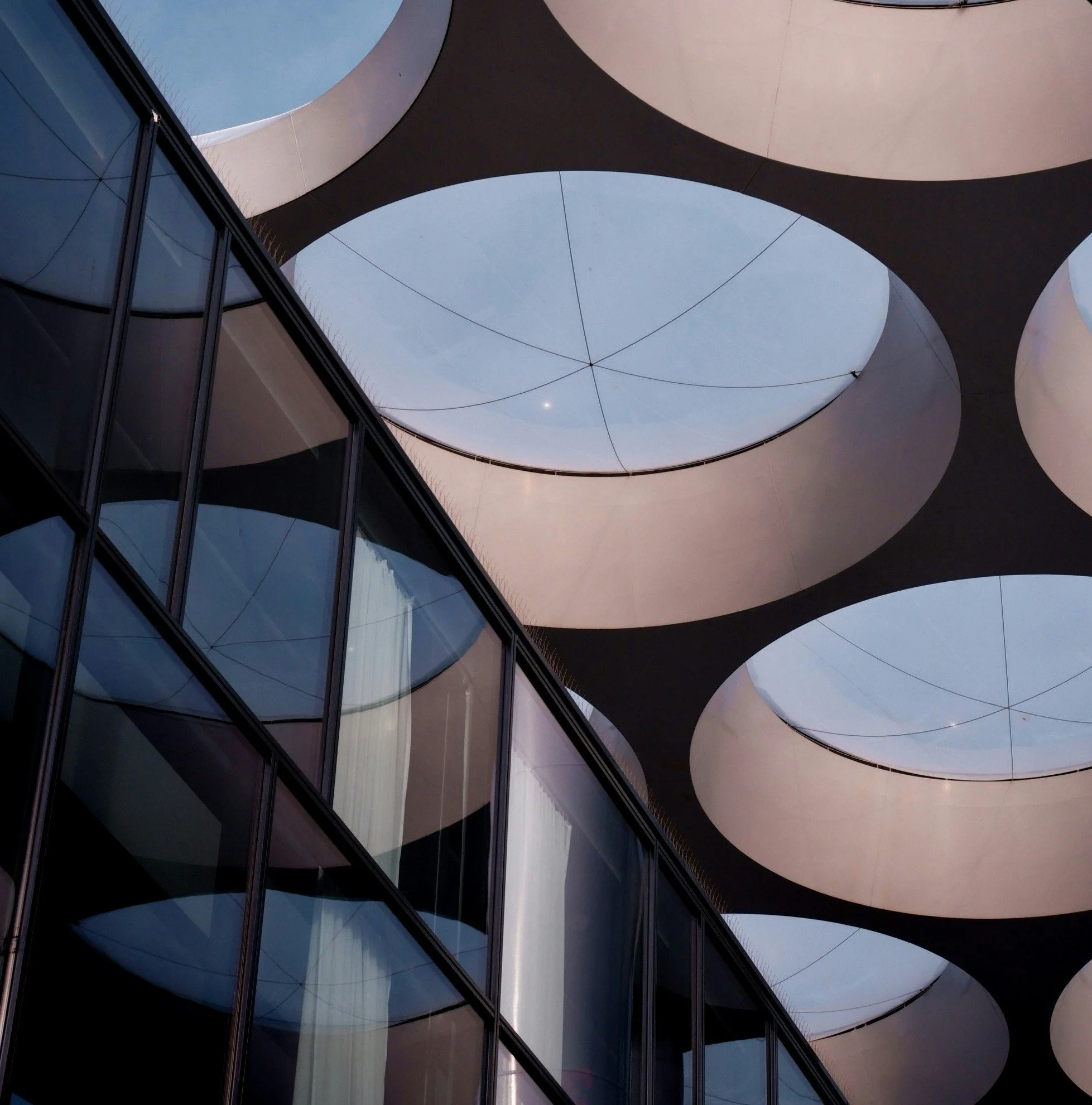 Looking up at the modern building's glass facade and circular openings in the ceiling, with clear sky visible through the openings.