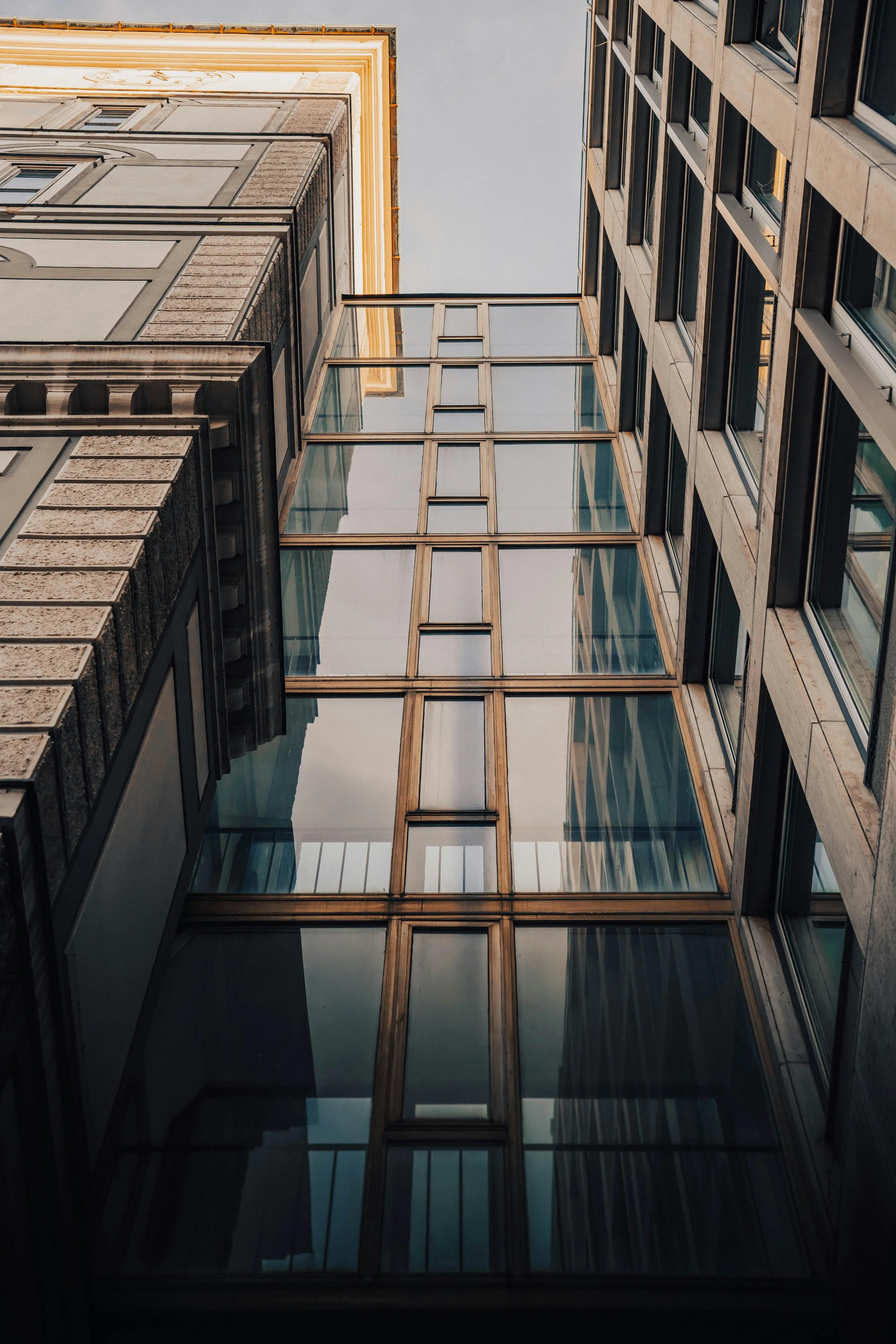 Looking up from the ground at the sky with tall buildings on either side, featuring glass and stone facades.