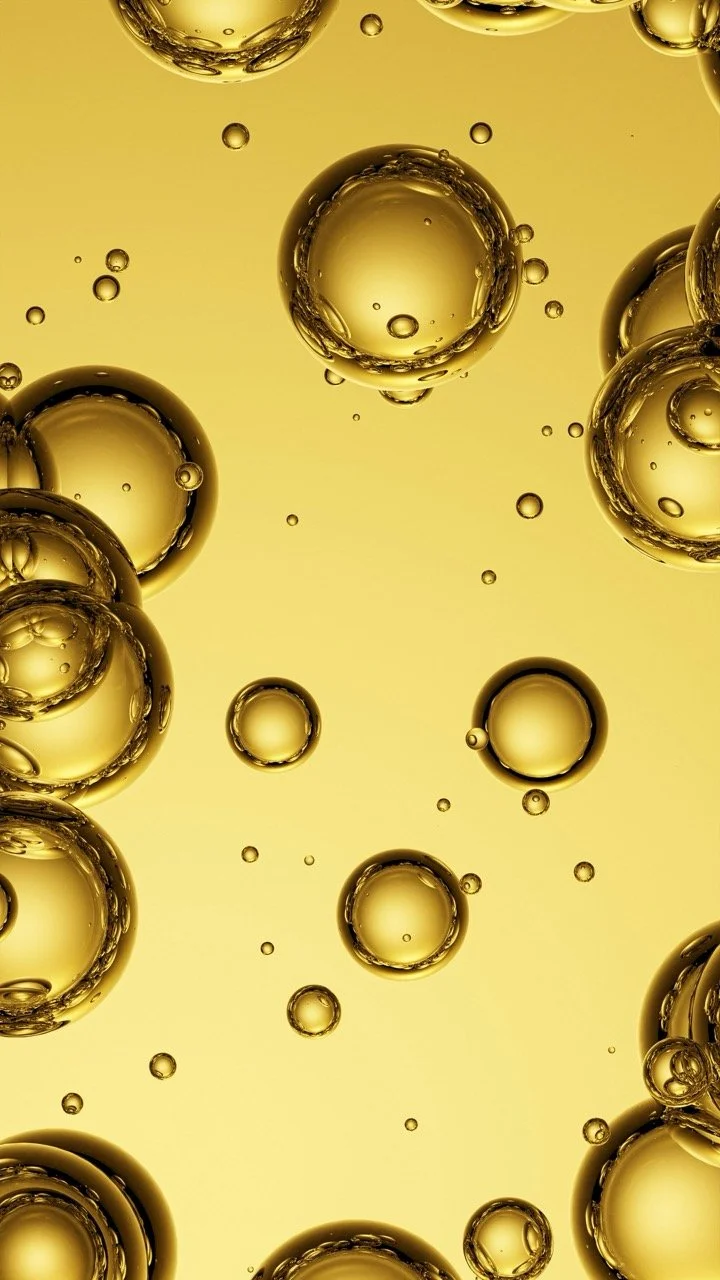 Nahaufnahme von Blasen in einer öligen Flüssigkeit, goldfarbene Tonalität, transparente Blasen
