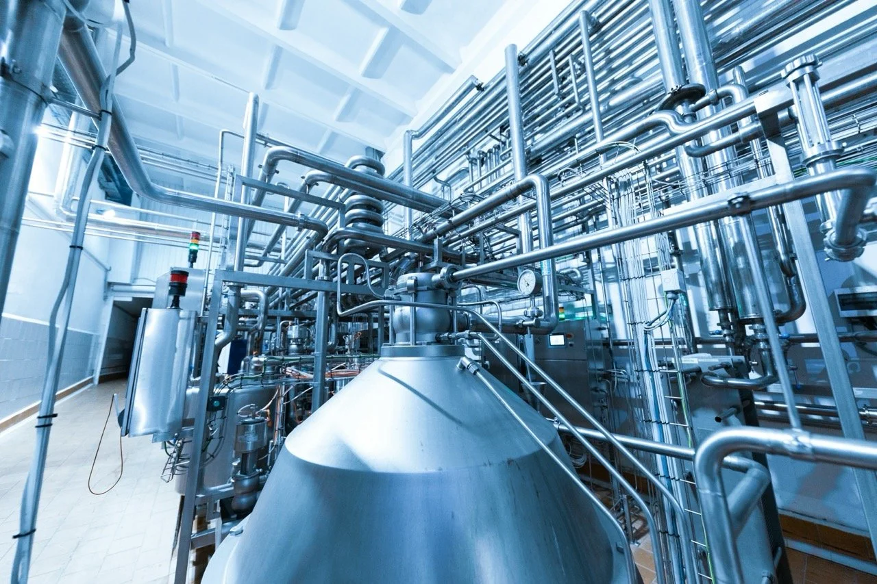 Stahlrohre und -behälter in einer Industrieanlage, wahrscheinlich in einer Fabrik oder einem Chemielabor.