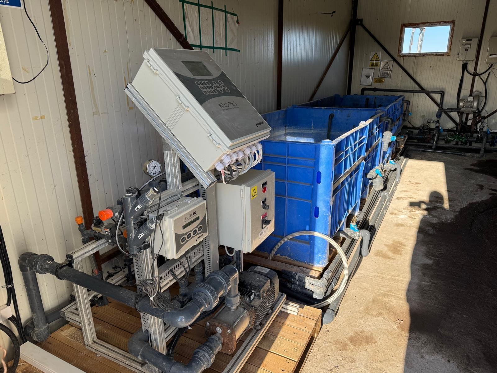 Industrial water treatment system with blue filtration tank, control panels, pipes, and gauges in a warehouse.