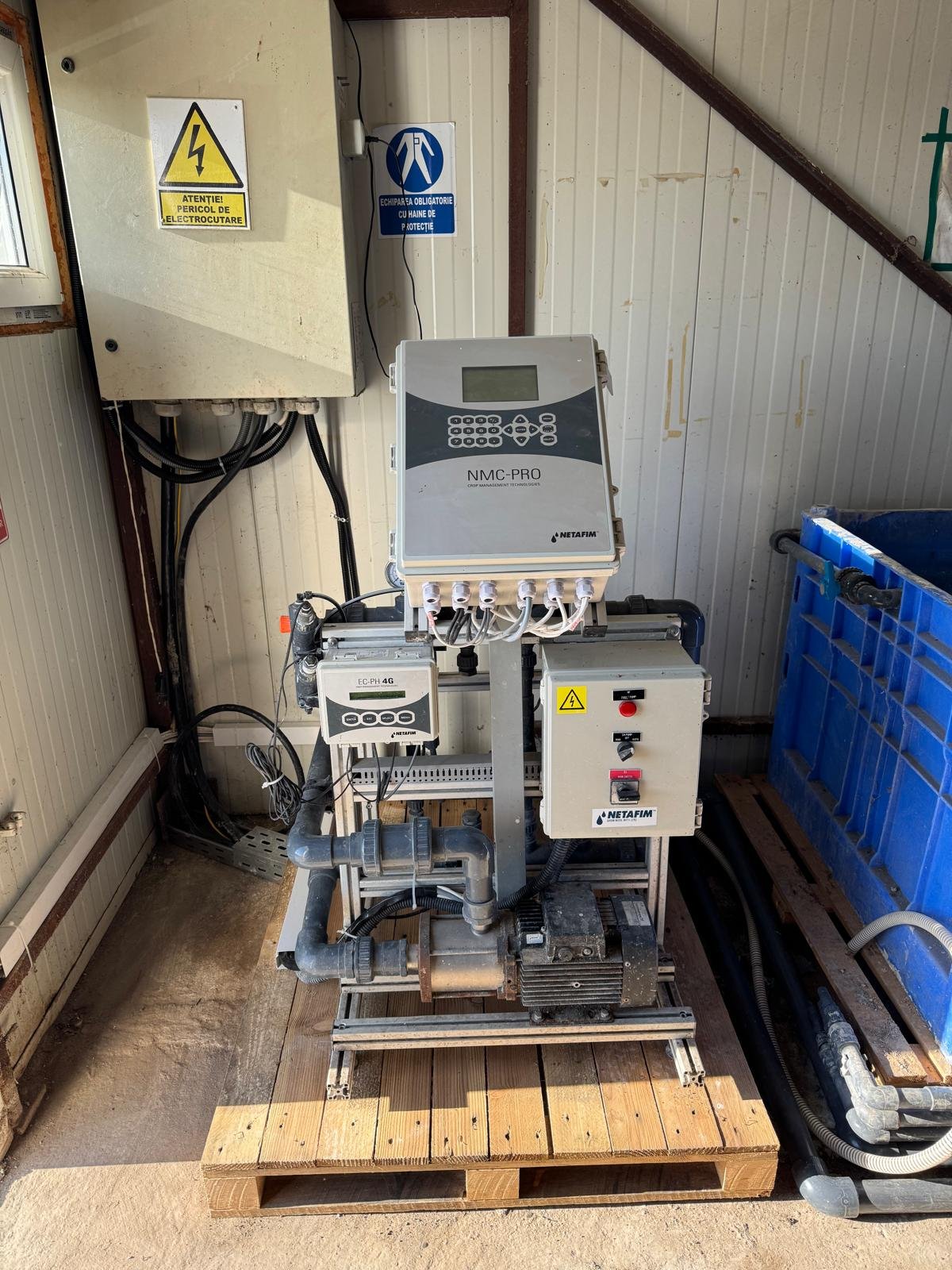 Industrial water pump system with control panels and piping on a wooden platform inside a building.